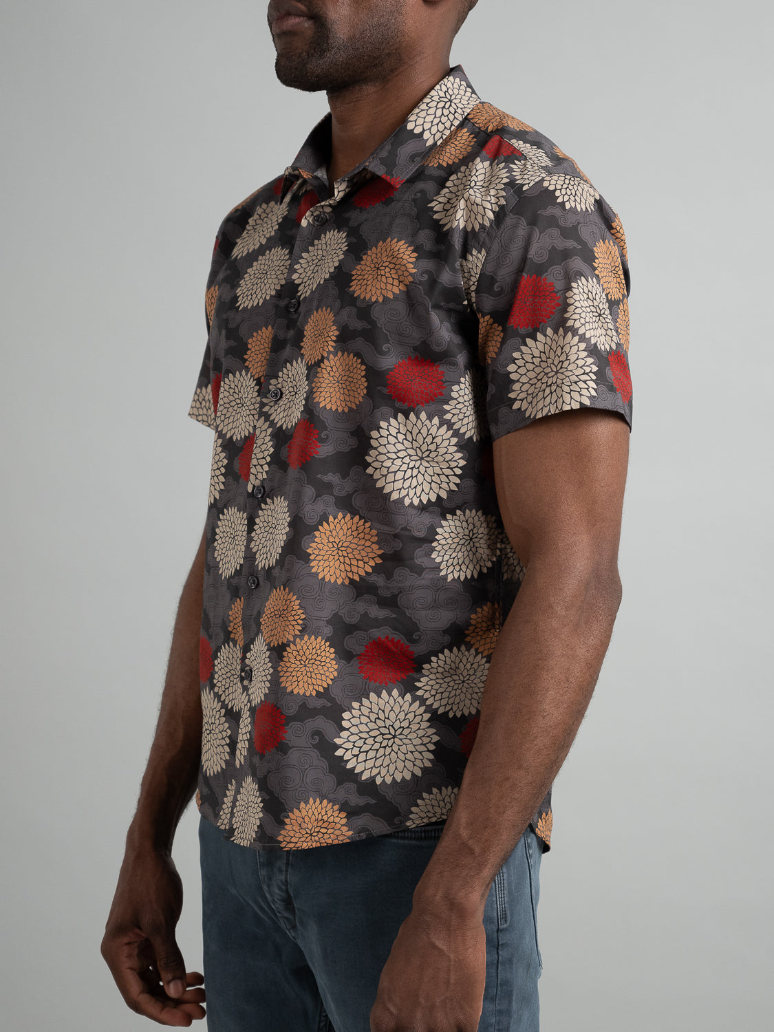 A person stands against a gray background wearing the Tibet Short Sleeve Cotton Printed Shirt by ID Menswear, featuring vibrant prints of red, beige, and gold flowers.