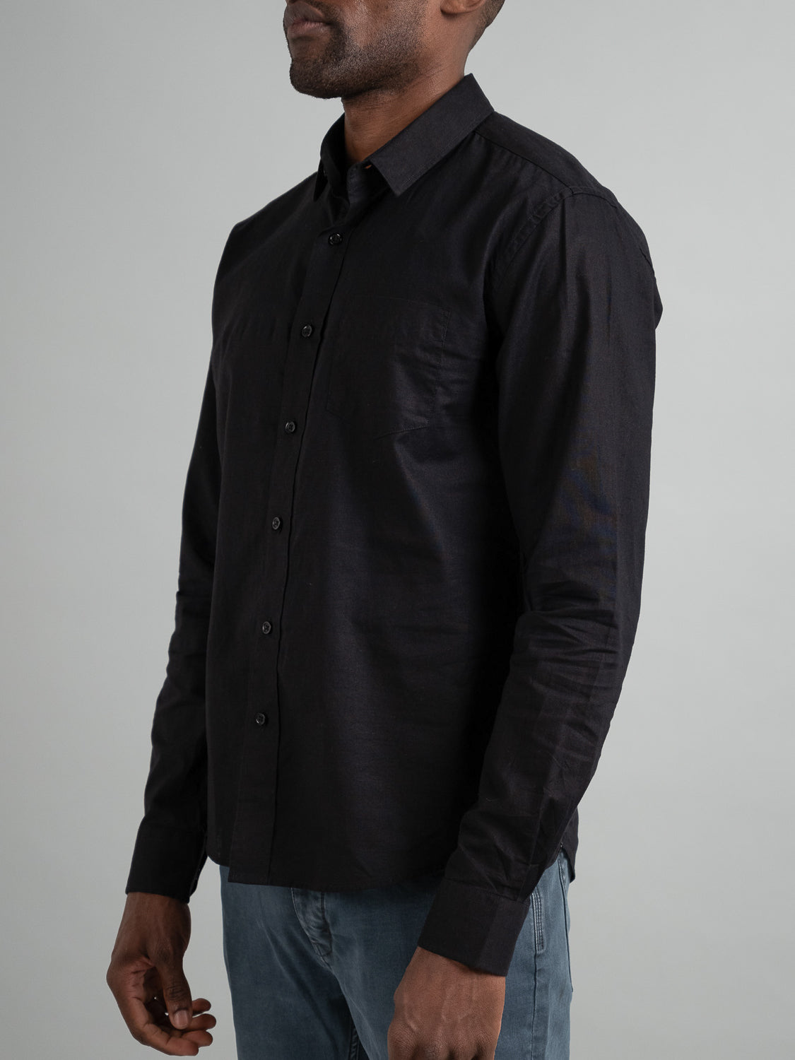 A person wearing an ID Menswear Goa Linen Cotton Long Sleeve Shirt and blue jeans stands against a gray background, with their face obscured, adding an air of mystery.