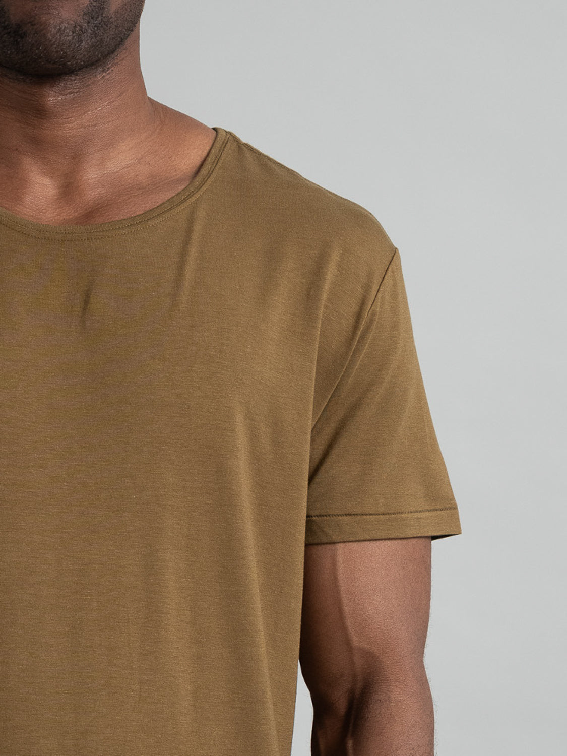 A person is shown wearing a short-sleeved, olive-green Slay Wide Neck Bamboo Blend Tee by ID Menswear from shoulder to waist against a plain background, highlighting its texture and stylish color.