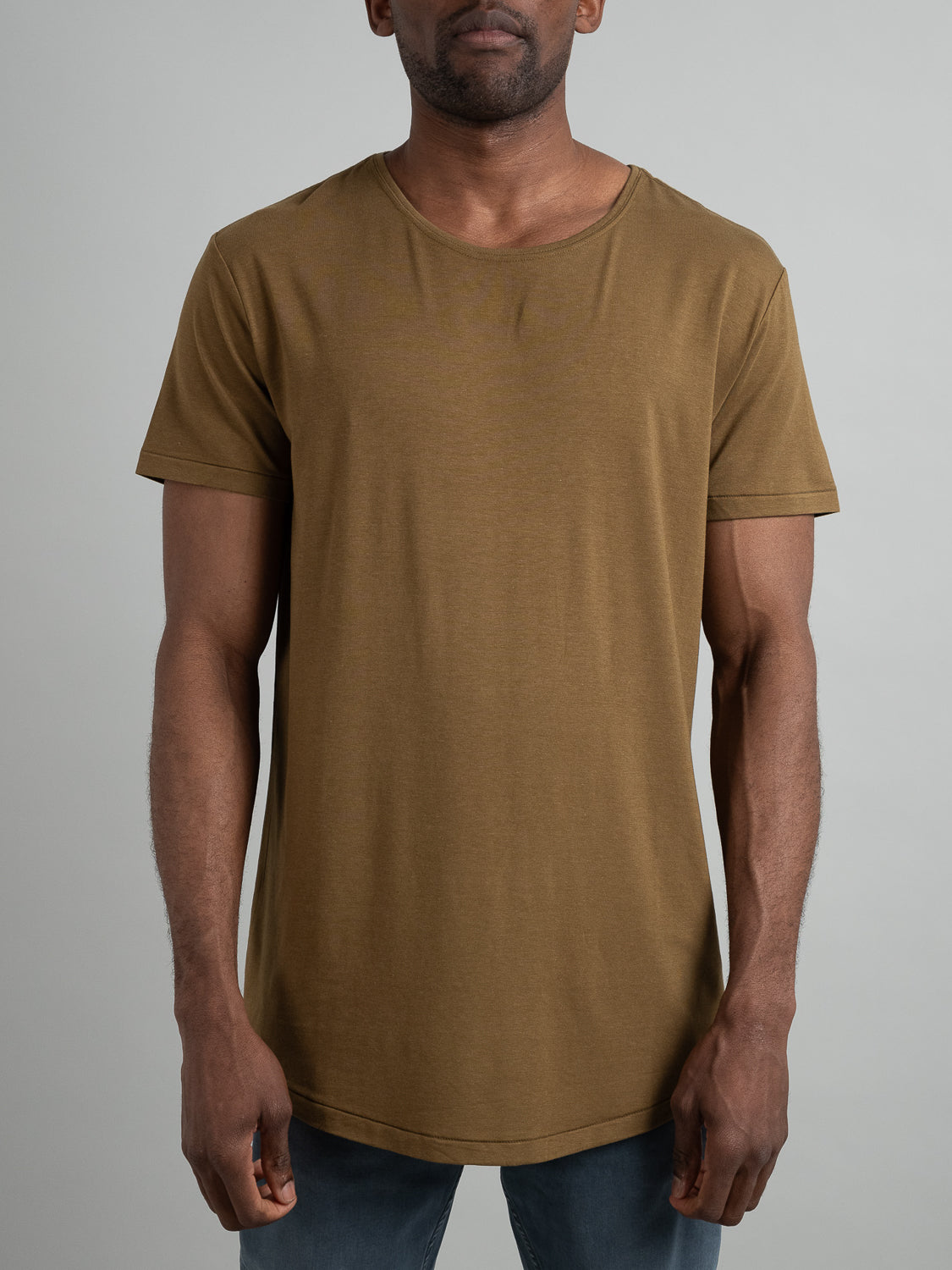 A person in an olive green Slay Wide Neck Bamboo Blend Tee from ID Menswear and blue jeans stands against a gray backdrop. The short-sleeve top, with its wide neckline, adds style to their unseen face.