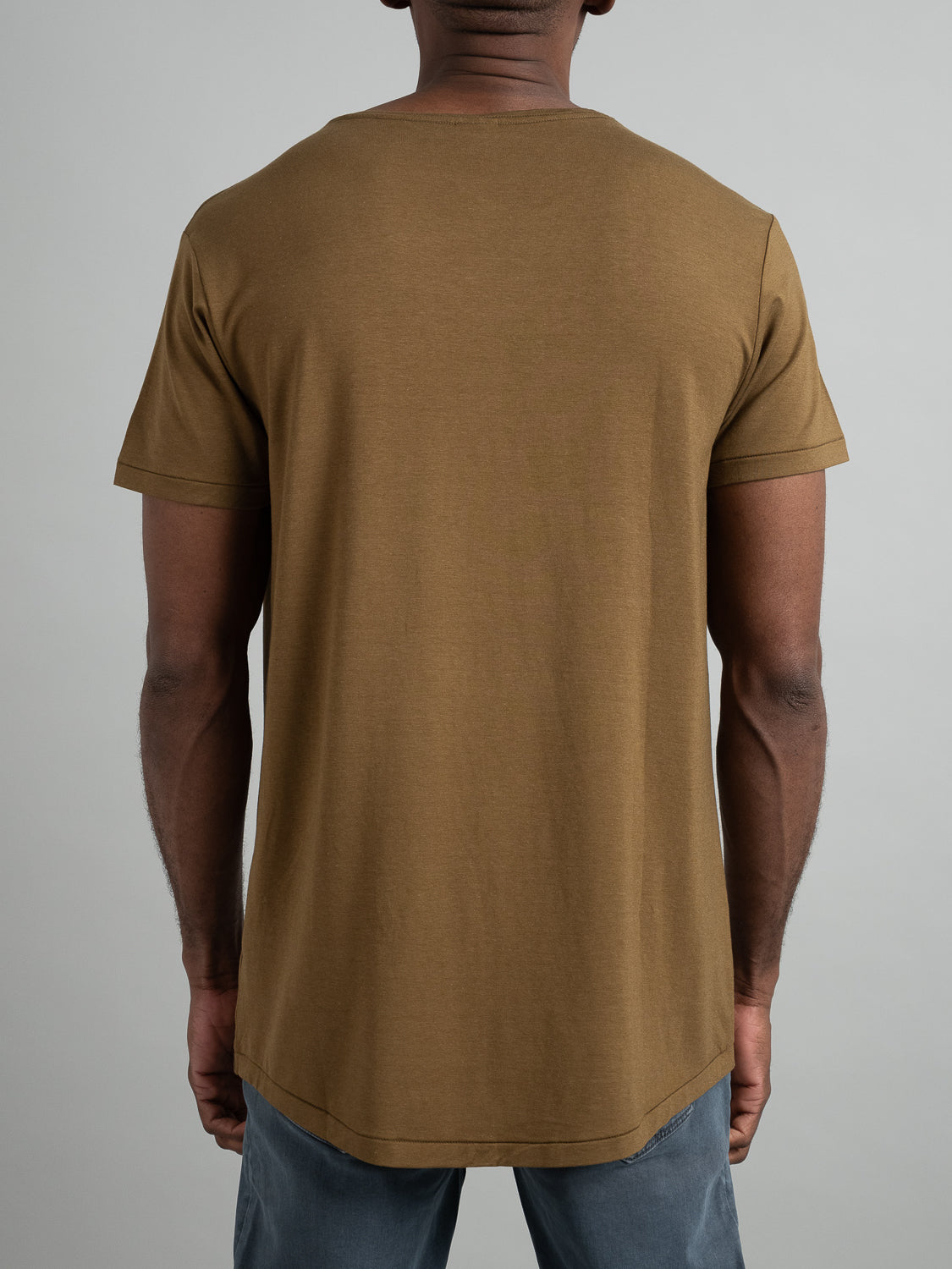 A person stands with their back to the camera, wearing a plain brown Slay Wide Neck Bamboo Blend Tee by ID Menswear and grey pants against a plain background.