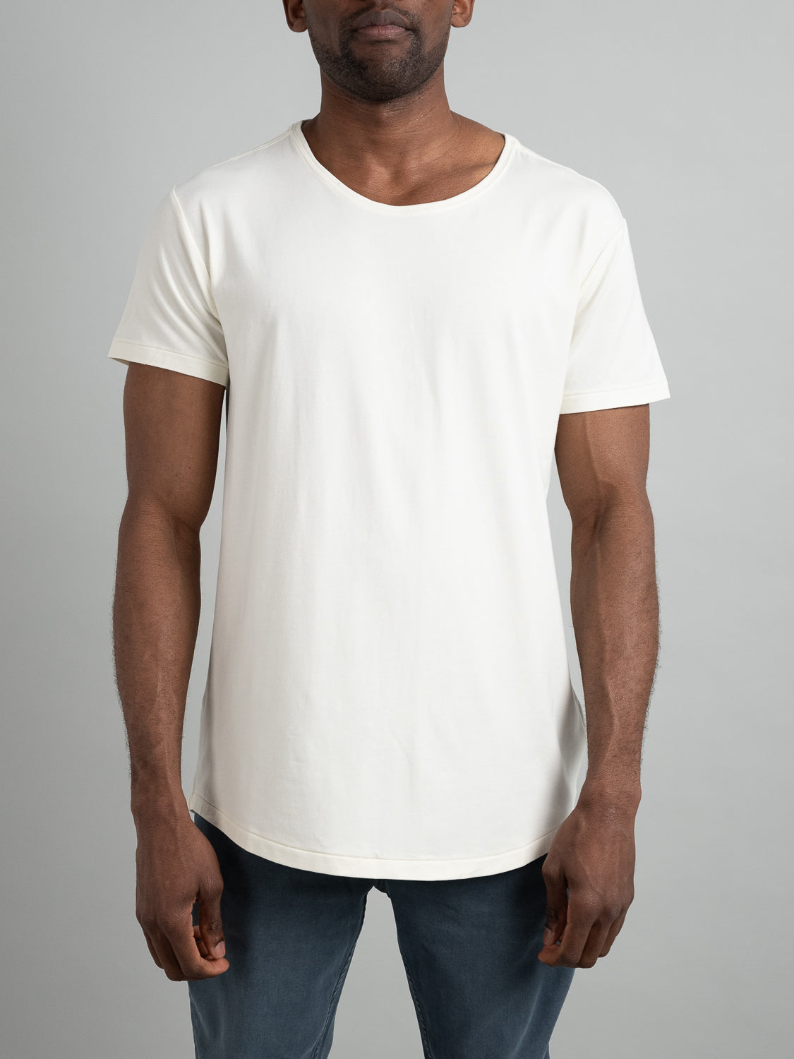 A man in a Slay Wide Neck Bamboo Blend Tee from ID Menswear and dark blue jeans stands against a gray background.