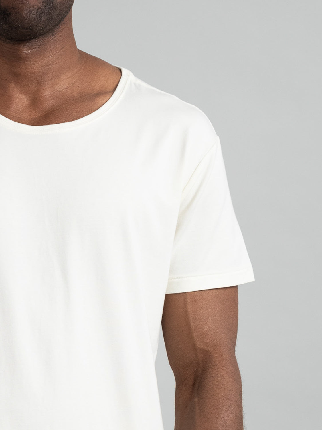 A person wearing an ID Menswear Slay Wide Neck Bamboo Blend Tee is shown from the upper body and arm against a gray background, highlighting the garments quality and comfort as sustainable fashion.