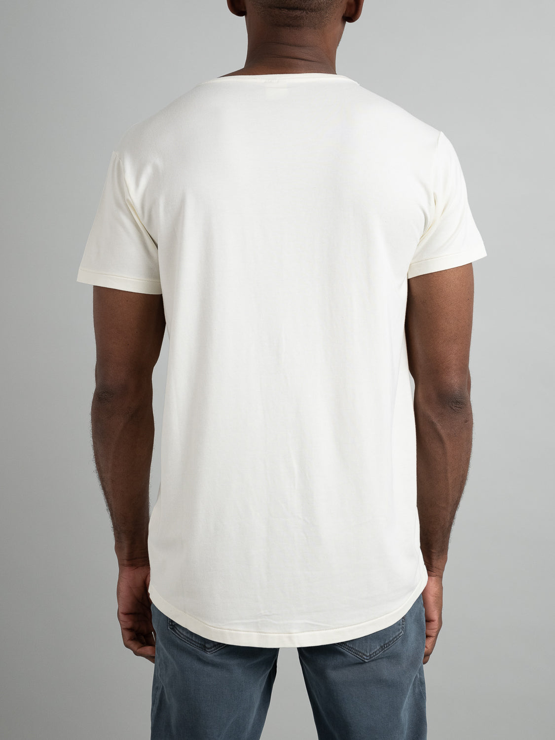 A person is wearing an ID Menswear Slay Wide Neck Bamboo Blend Tee, facing away from the camera against a gray background. They also have on blue jeans.