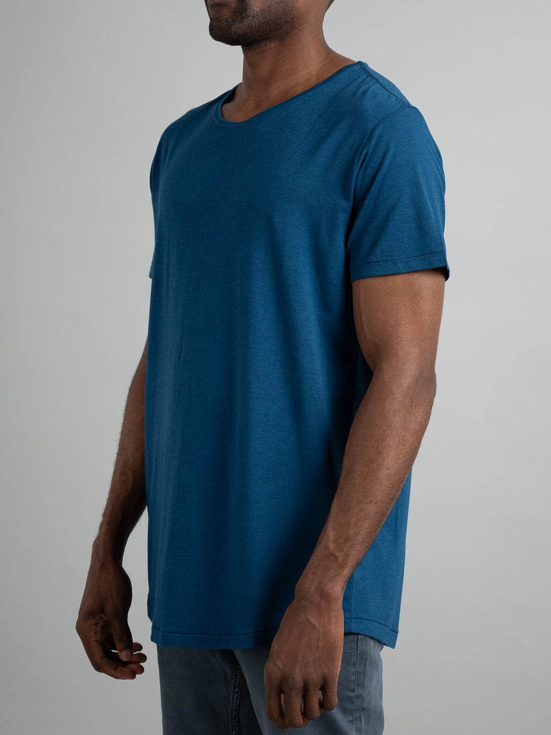 An individual in an ID Menswear Slay Wide Neck Bamboo Blend Tee and light gray pants stands against a plain background. The image highlights the tees short sleeves and loose fit from the neck down.