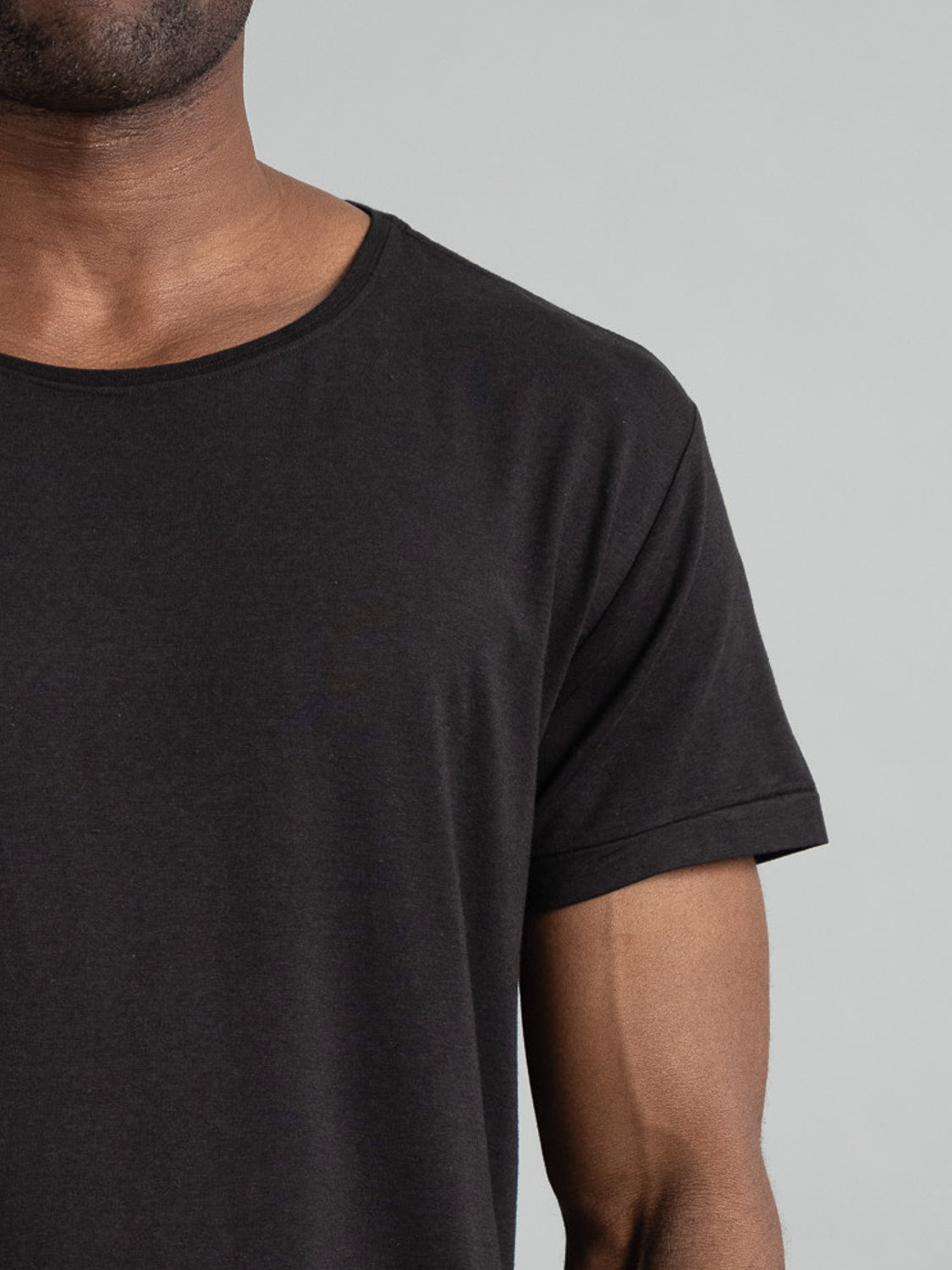 Close-up of a person in a Slay Wide Neck Bamboo Blend Tee by ID Menswear, featuring short sleeves and a round neckline, highlighted against a neutral gray background.