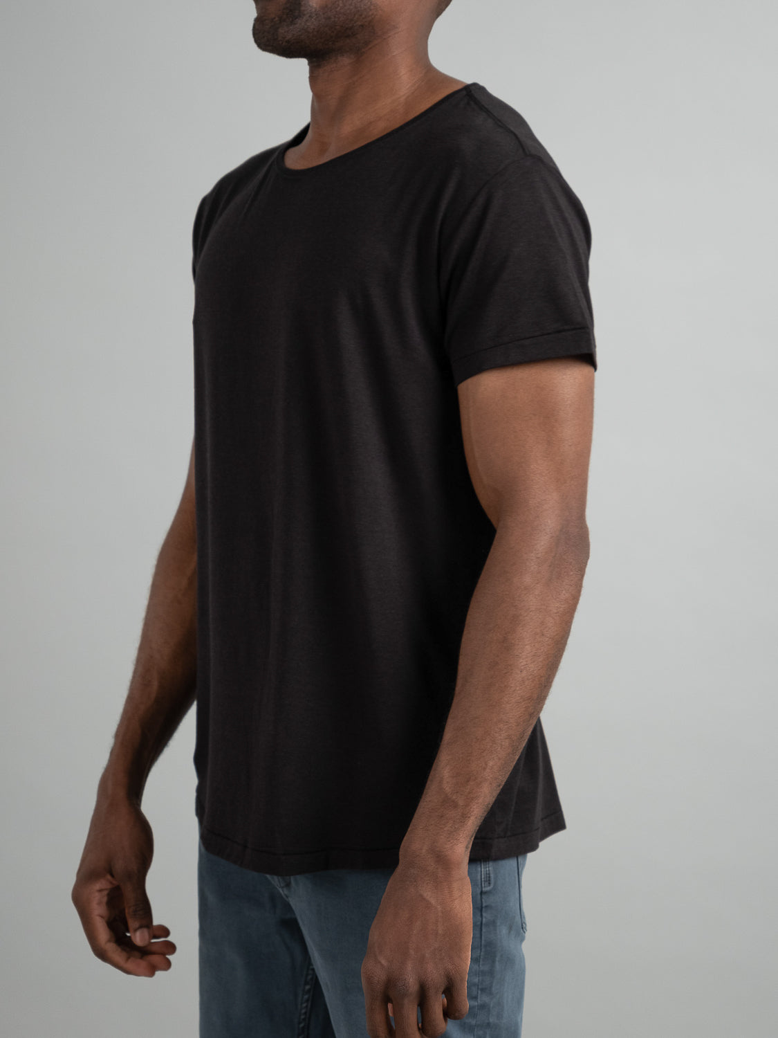 Someone in blue jeans stands against a light gray background wearing an ID Menswear Slay Wide Neck Bamboo Blend Tee. The image is cropped at the head, with their arms at their sides.