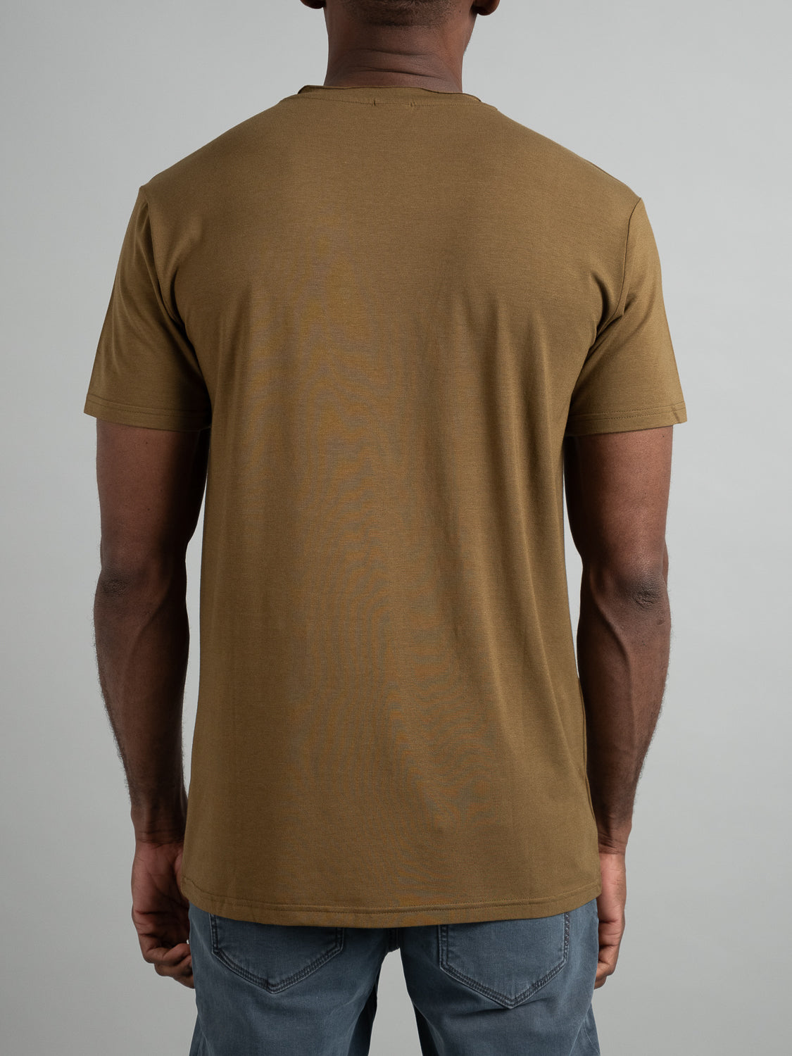 An individual is pictured from behind in a brown Bello Bamboo Blend Rolled Neck Tee by ID Menswear and blue jeans, set against a plain gray backdrop.