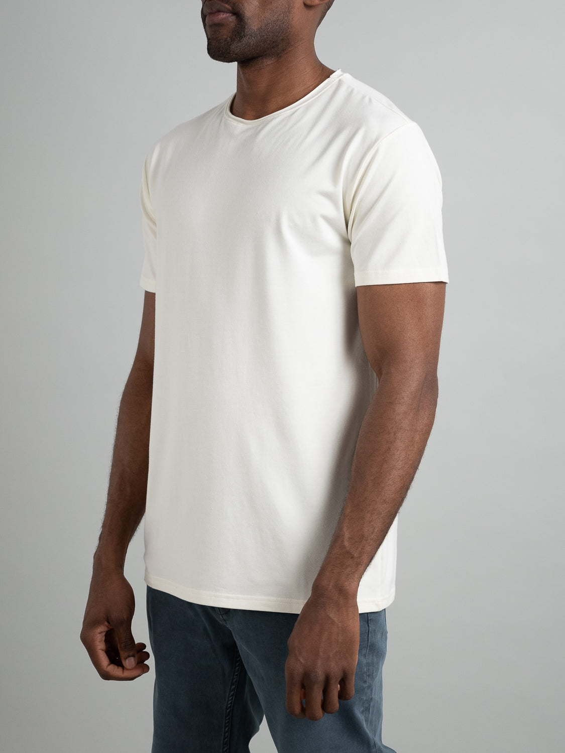A person wearing an ID Menswear Bello Bamboo Blend Rolled Neck Tee and blue jeans stands against a neutral background, facing slightly to the left with relaxed arms by their sides.