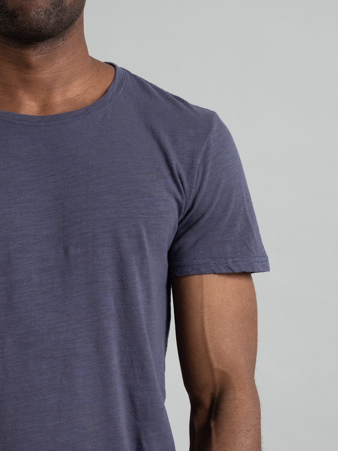 A person is shown from the shoulders down wearing the Mini Flip Slub Yarn Tee by ID Menswear, a plain dark blue slub cotton t-shirt, against a light gray background. The image highlights the shirts texture, ideal for an everyday casual look.