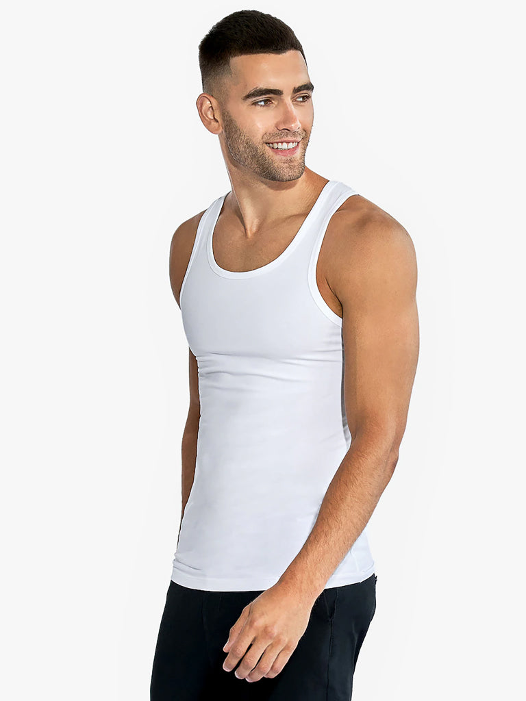 A man stands against a plain background, donning a Bread & Boxer 2 Pack Cotton Stretch Tank Top and black pants. With short dark hair and a trimmed beard, he gazes left with a smile, effortlessly embodying comfort and style in this perfect base layer ensemble.