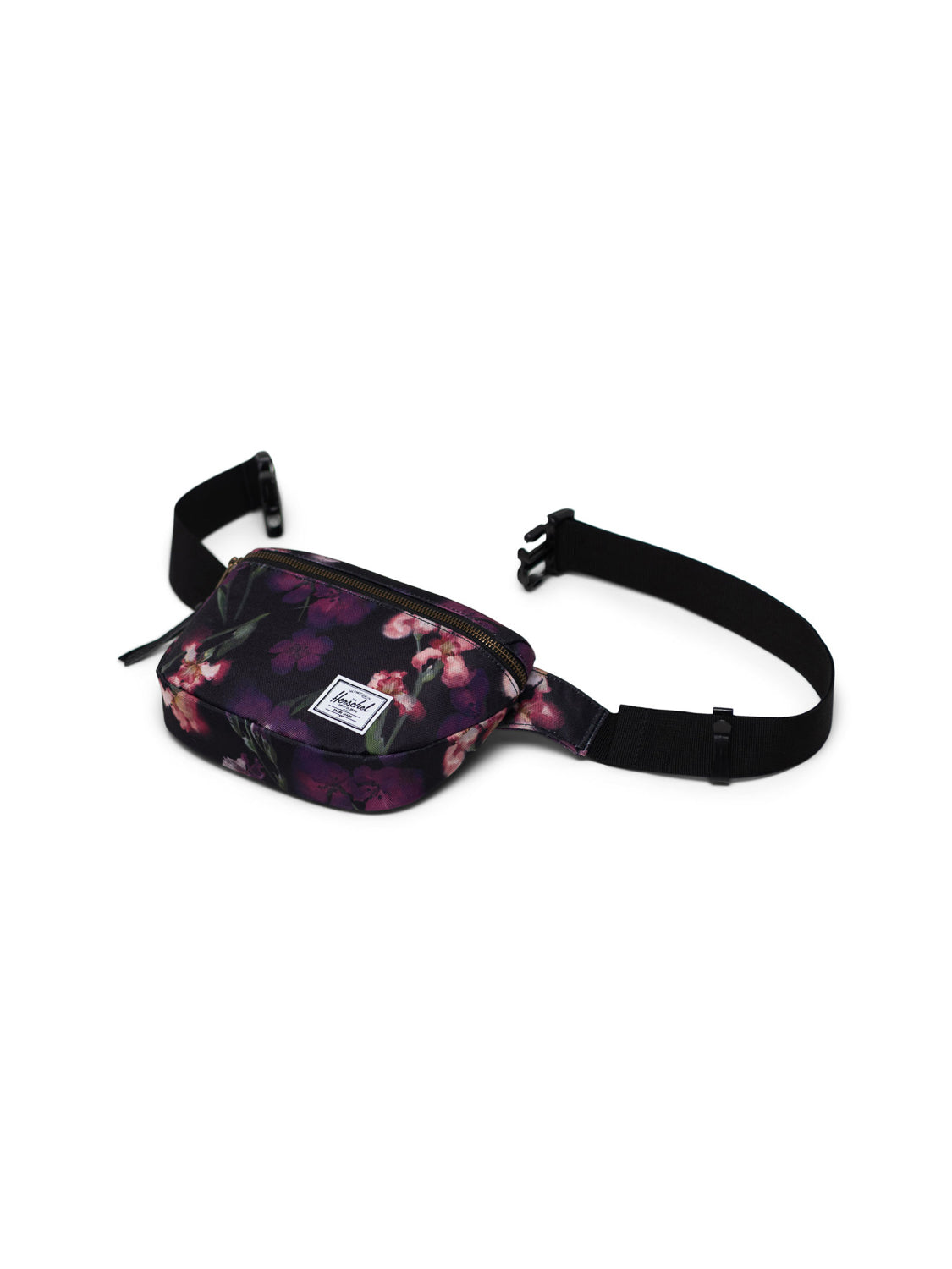 The Herschel Fifteen Hip Pack features a black design with a pink and purple floral pattern, metal zipper front pocket, adjustable black strap, and a small white rectangular brand label on the front.