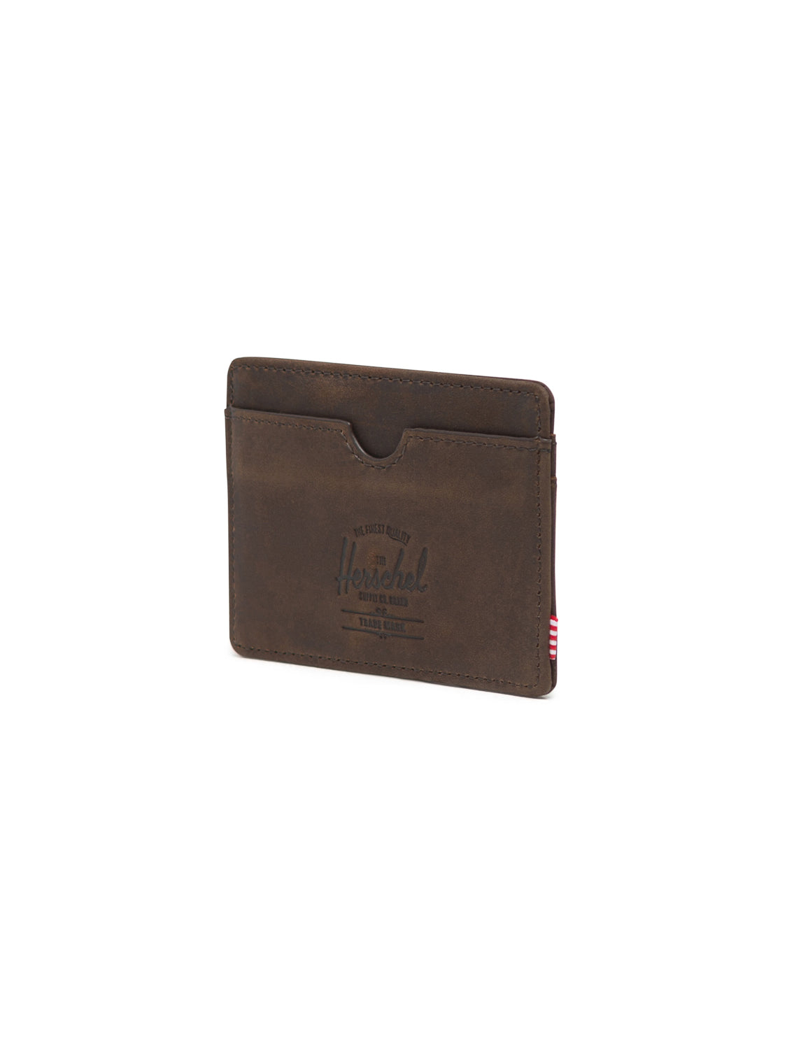 The Herschel Charlie Leather Card Holder Wallet features a brown leather finish, central pocket, embossed front logo, and a red and white striped side tag, shown on a white background.