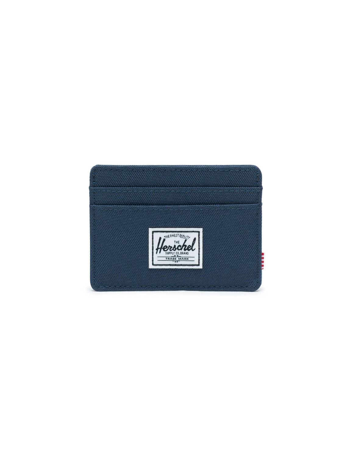 The Herschel Charlie Compact Card Holder Wallet is navy blue with RFID blocking, three card slots, and a white rectangular Herschel Supply Co. label on the front, shown against a white background.