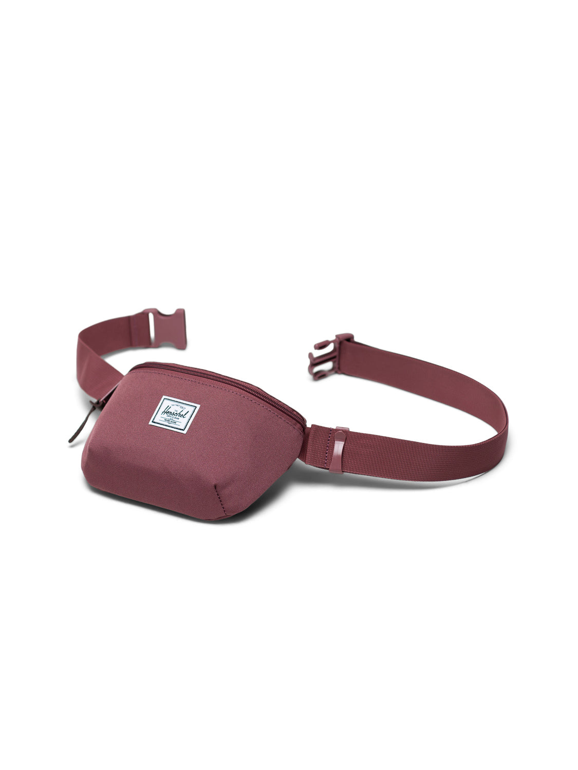 The Herschel Fourteen Hip Pack in maroon features an adjustable strap with buckle, a zippered main compartment, and a small white rectangular logo patch on the front. The bag is shown against a white background.