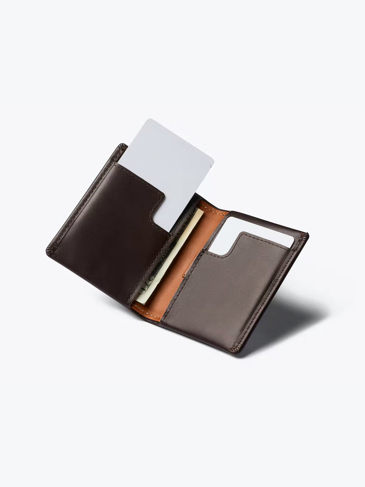 The Bellroy Slim Sleeve Wallet in open dark brown shows two card slots—one with a white card, one empty—and a compartment holding paper currency, all displayed on a light gray background for a pocket-friendly look.