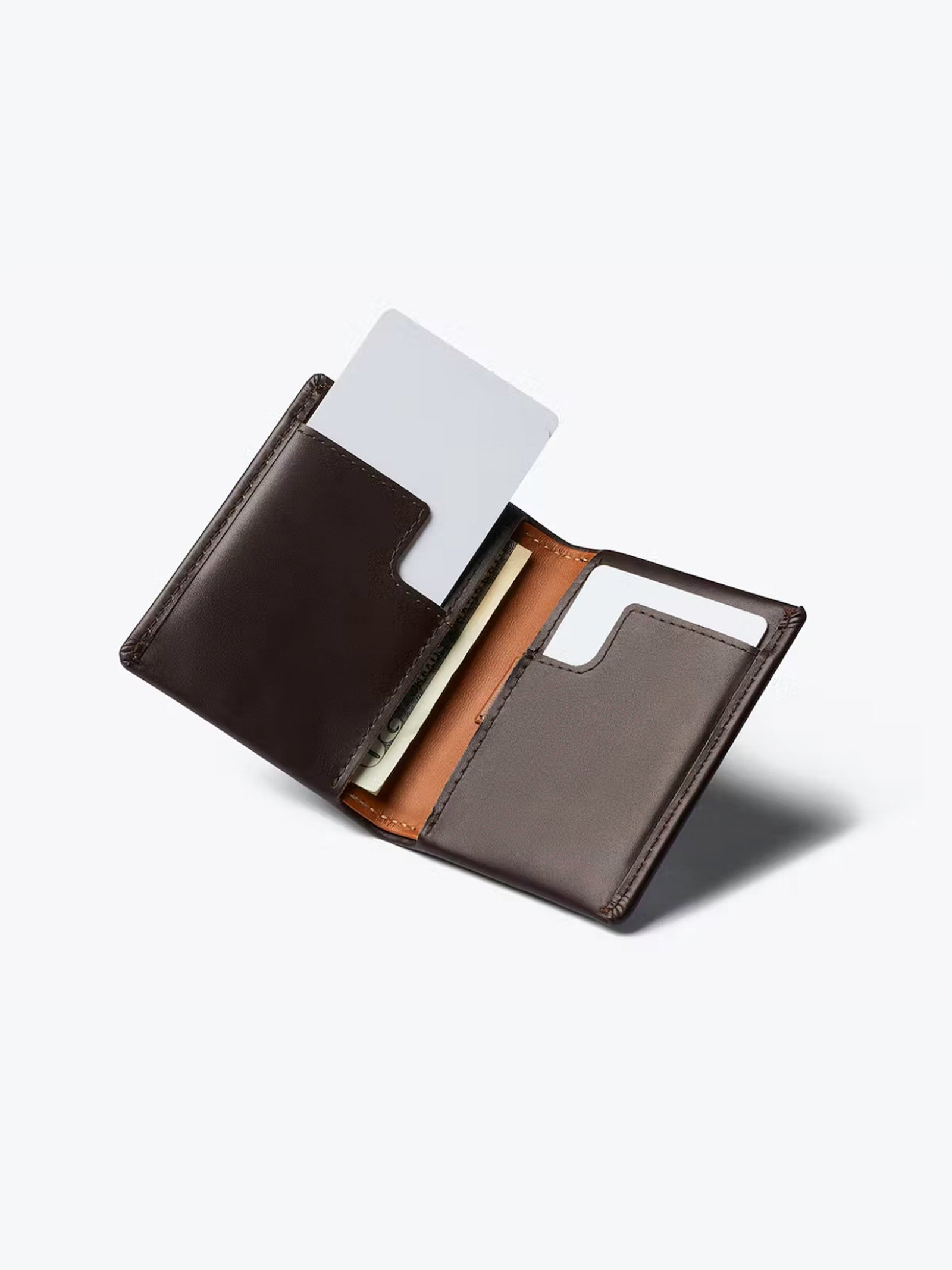 The Bellroy Slim Sleeve Wallet in open dark brown shows two card slots—one with a white card, one empty—and a compartment holding paper currency, all displayed on a light gray background for a pocket-friendly look.