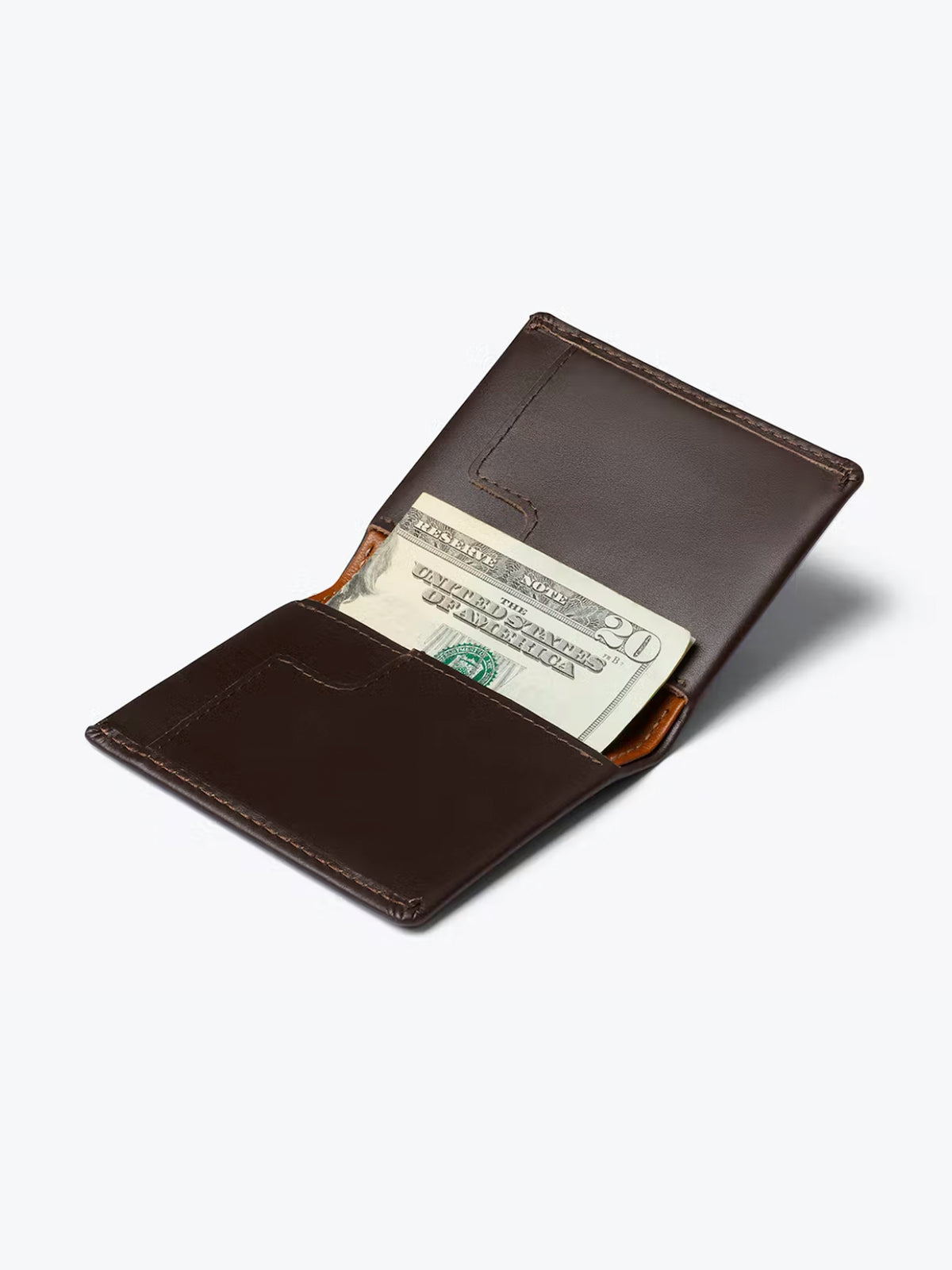 A dark brown Bellroy Slim Sleeve Wallet lies open against a light background, with a visible twenty-dollar bill partially tucked into one of its inner pockets.