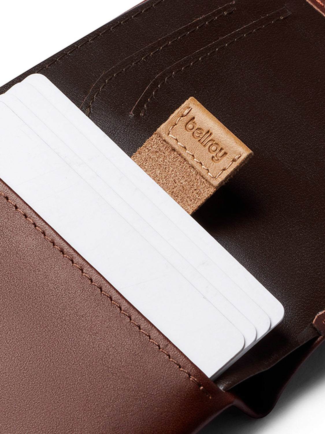 A close-up of the Bellroy Note Sleeve Wallet in brown leather, holding several white cards, with a tan pull tab labeled Bellroy visible inside.