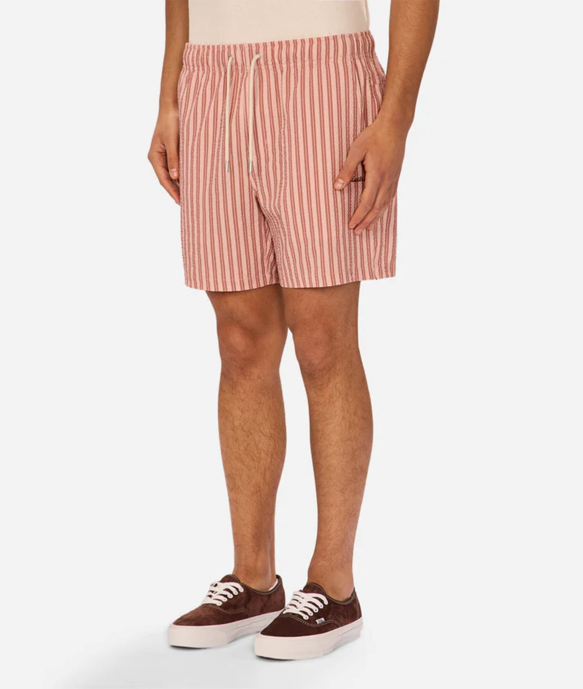A person stands against a plain background wearing Industrie’s Berkeley Swim Short, featuring red and white vertical stripes and a drawstring, paired with brown sneakers with white soles.