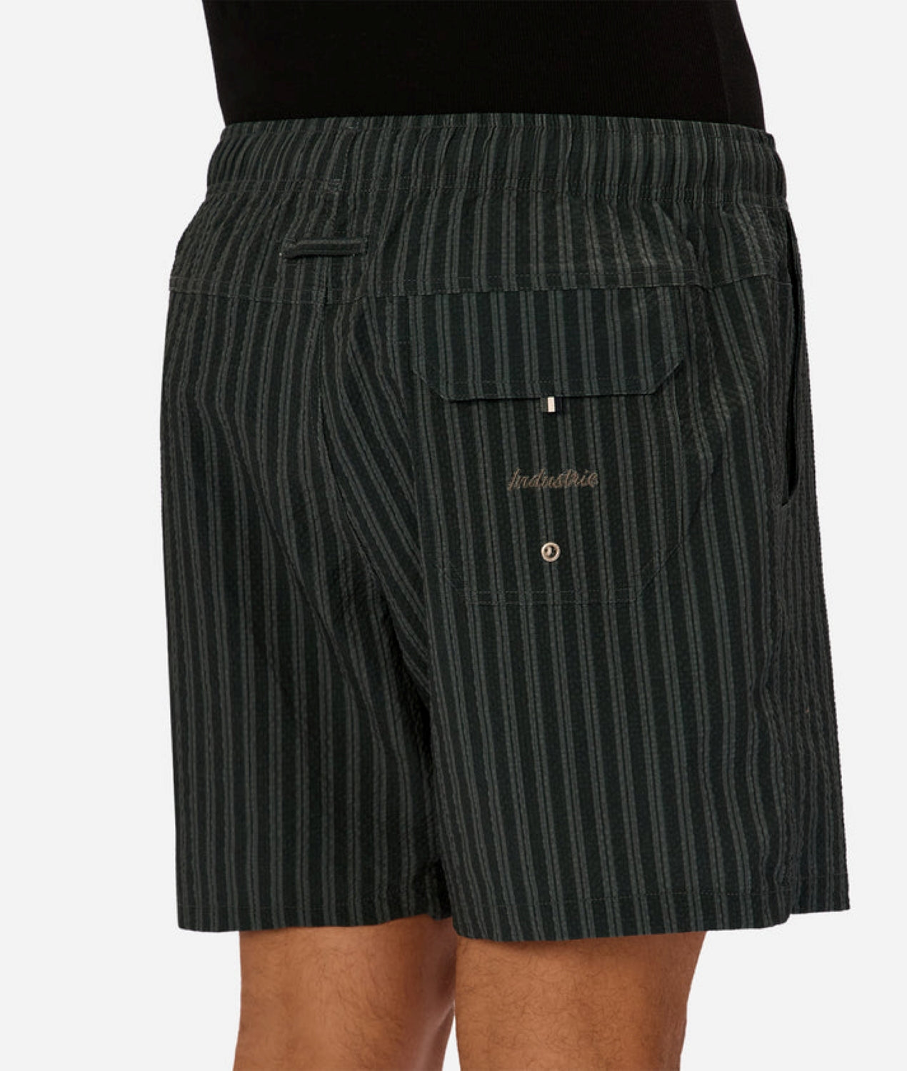A person wearing Berkeley Swim Shorts by Industrie, featuring black and grey pinstripes, an elastic waistband, and a back pocket with a button and embroidered Industrie branding.