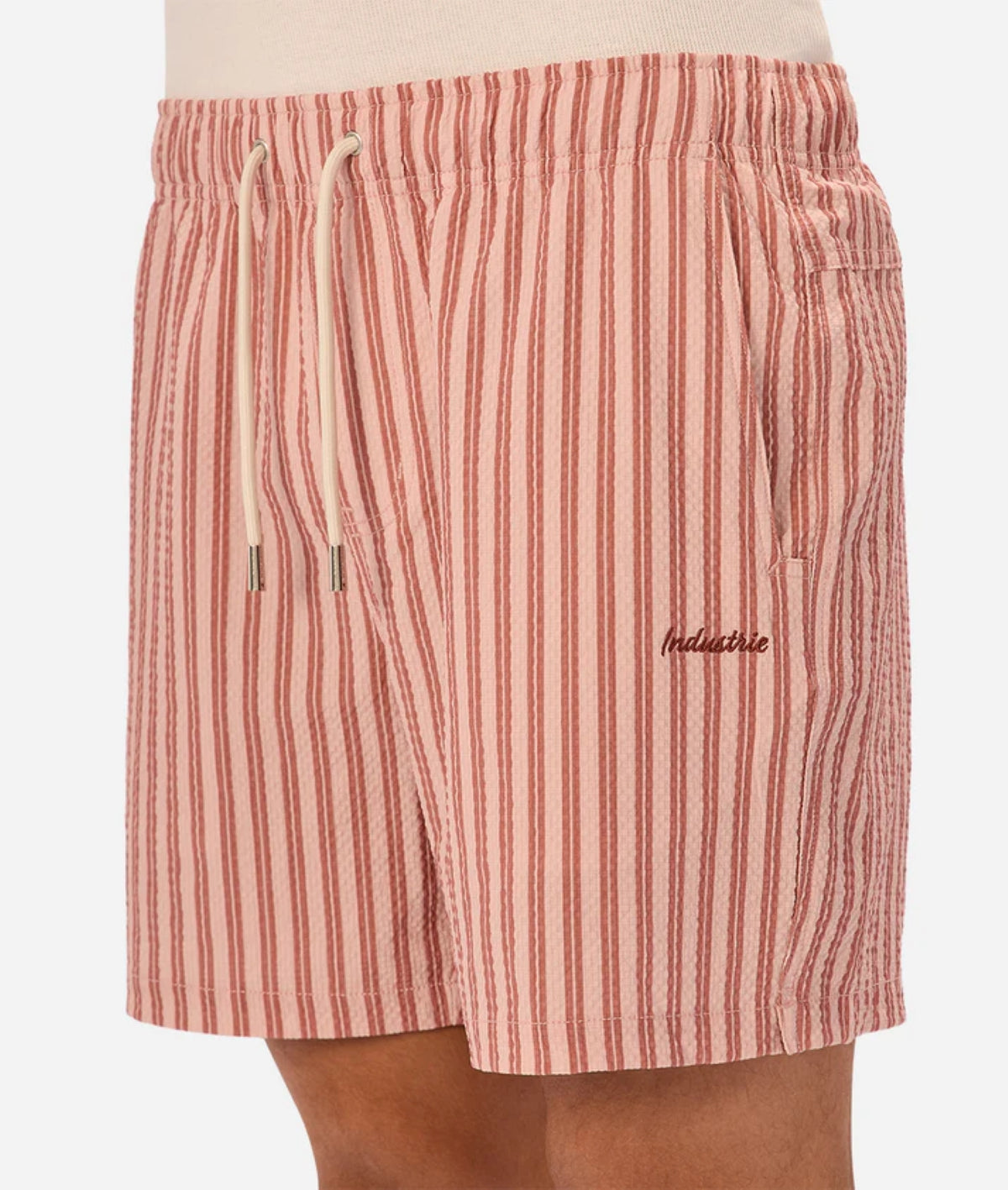 Someone wears the Industrie Berkeley Swim Short—pink and white vertical stripes, seersucker fabric, drawstring waist, pockets, and "Indacloud" embroidered on the left leg.