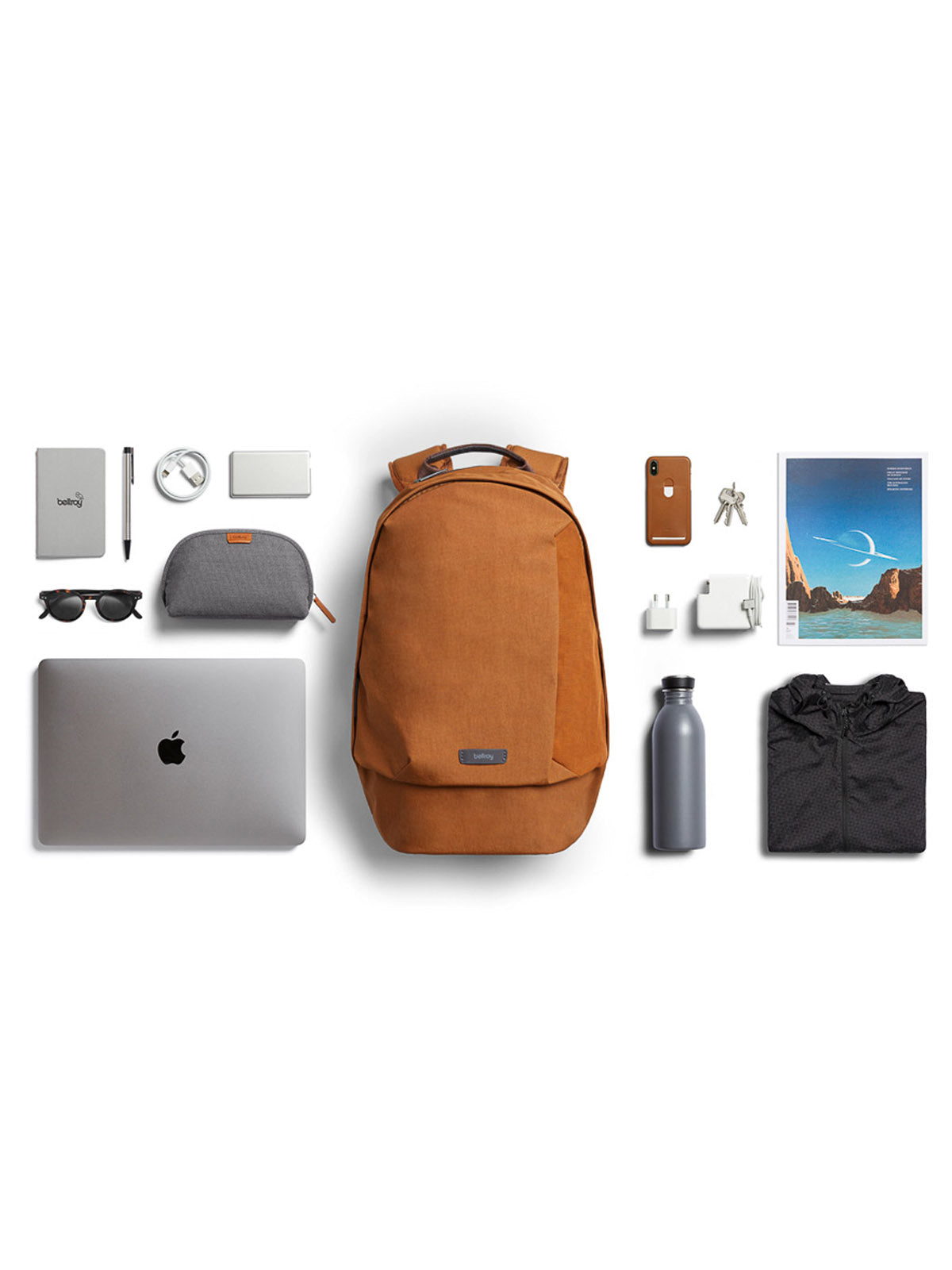 A neatly arranged flat lay showcases the Bellroy Classic Backpack - 20L with everyday essentials including a laptop, notebook, sunglasses, pens, charger, keys, phone, pouches, water bottle, and a travel magazine.