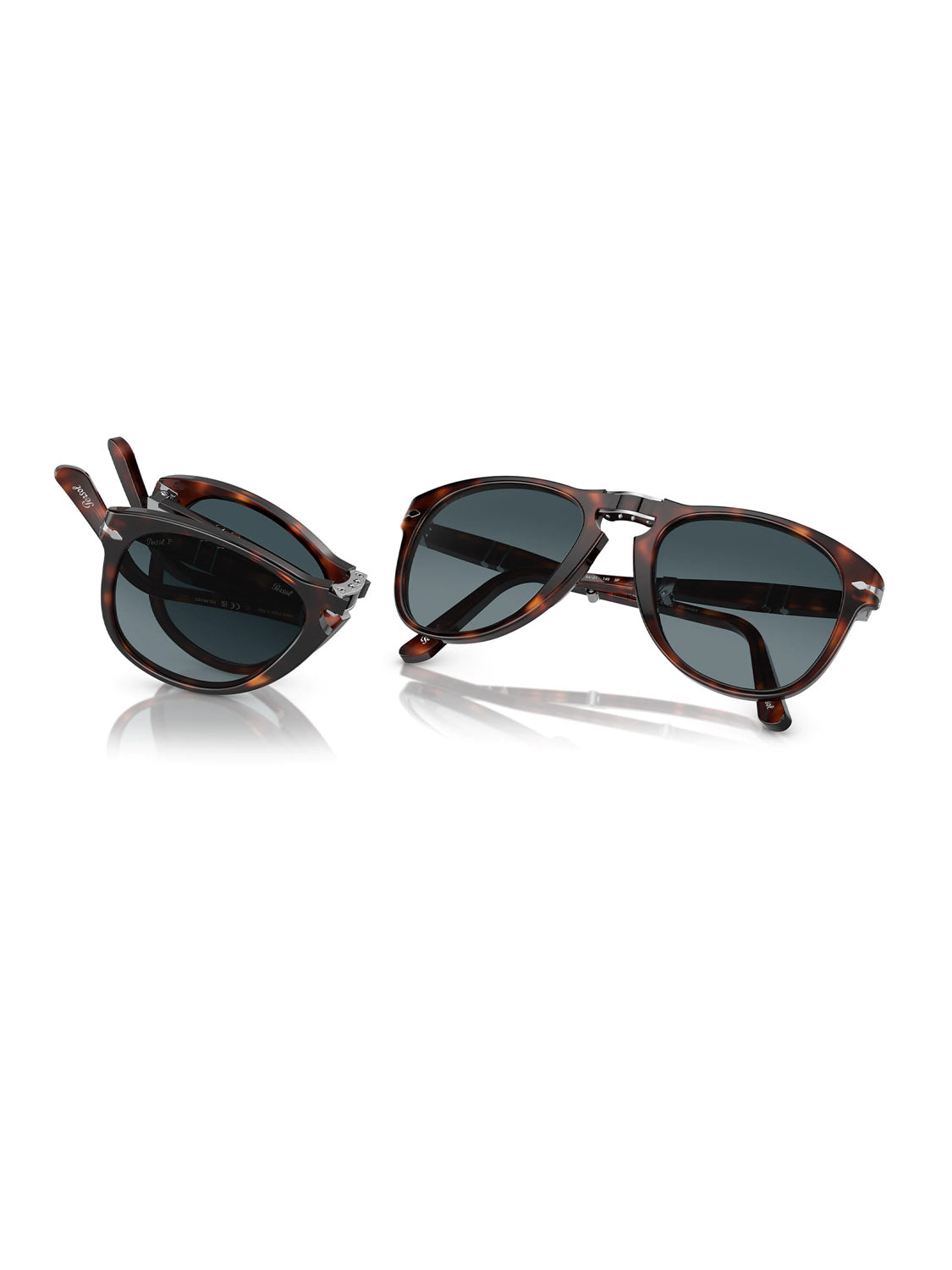 Two pairs of Persol PO714 sunglasses are on a white background. One pair, open with an acetate tortoiseshell frame and dark lenses, exudes elegance. The other, folded in the same stylish design, gleams brilliantly with its crystal polarized lens reflecting light.