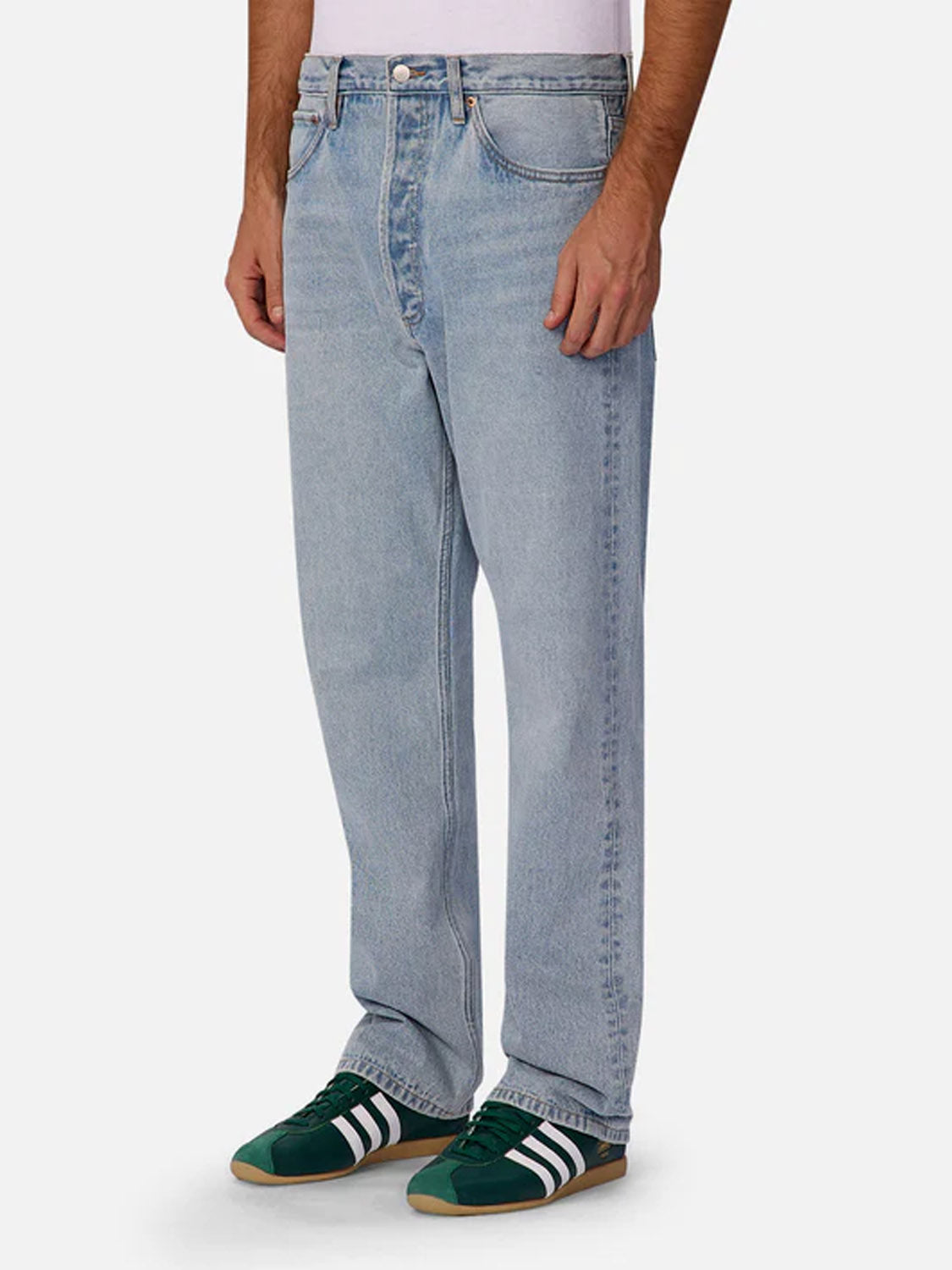Someone is standing against a plain white background wearing Industrie 90s Jean Stone Wash straight leg jeans, a white shirt, and green Adidas sneakers with white stripes.