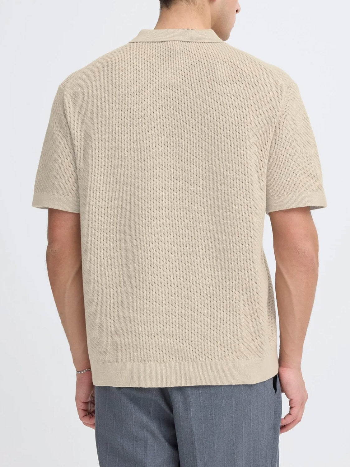 A person stands facing away, wearing the Casual Friday Cfisaksson Polo Knit in beige with gray pinstripe pants against a plain light background.