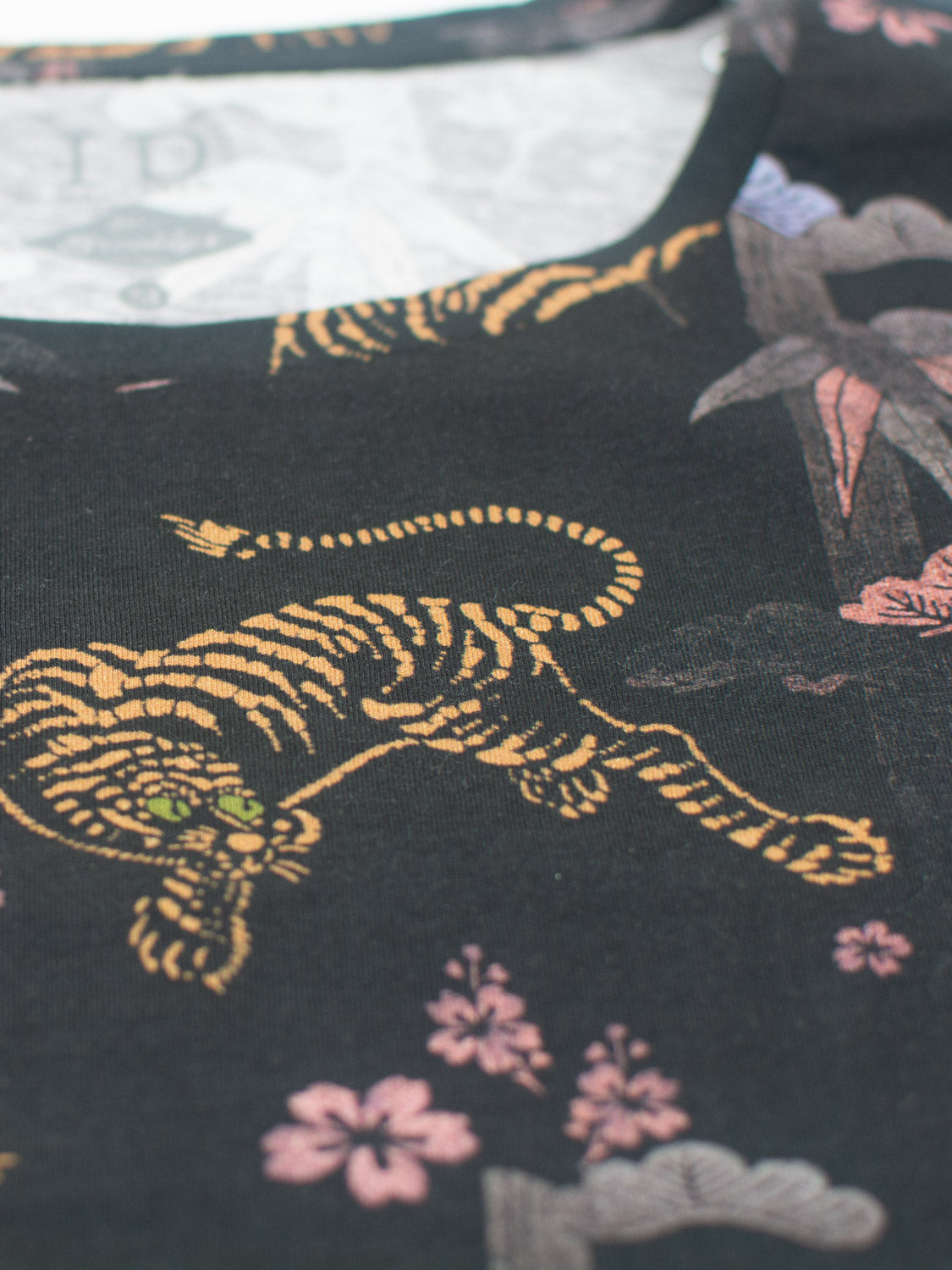 Close-up of a black Bali Vintage Japanese Print Tee by ID Menswear, made from organic cotton, featuring a vibrant design with a yellow leaping tiger with green eyes amidst pink flowers, mimicking a vintage Japanese print.