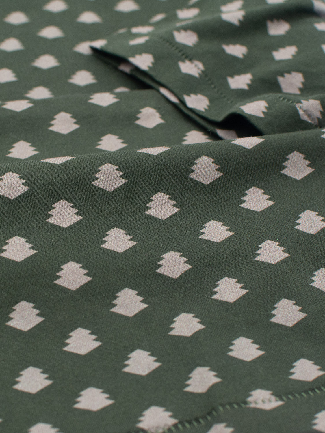 Close-up of the Bali Vintage Japanese Print Tee by ID Menswear, made from green organic cotton with a geometric pattern of small, light-colored diamonds. Visible stitching and subtle folds create a textured look inspired by vintage Japanese prints.