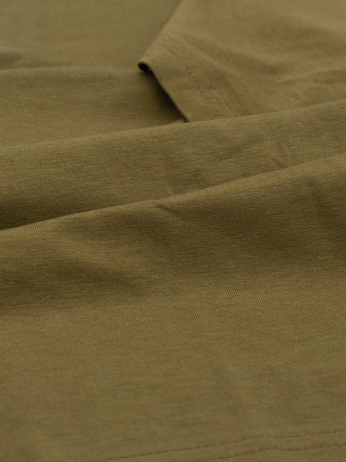 Close-up of a soft, olive green fabric with subtle folds, highlighting its smooth texture and gentle draping. This lightweight material, part of the Bello Bamboo Blend Rolled Neck Tee by ID Menswear, is sustainable and comfortable for organic cotton t-shirts or elegant curtains.