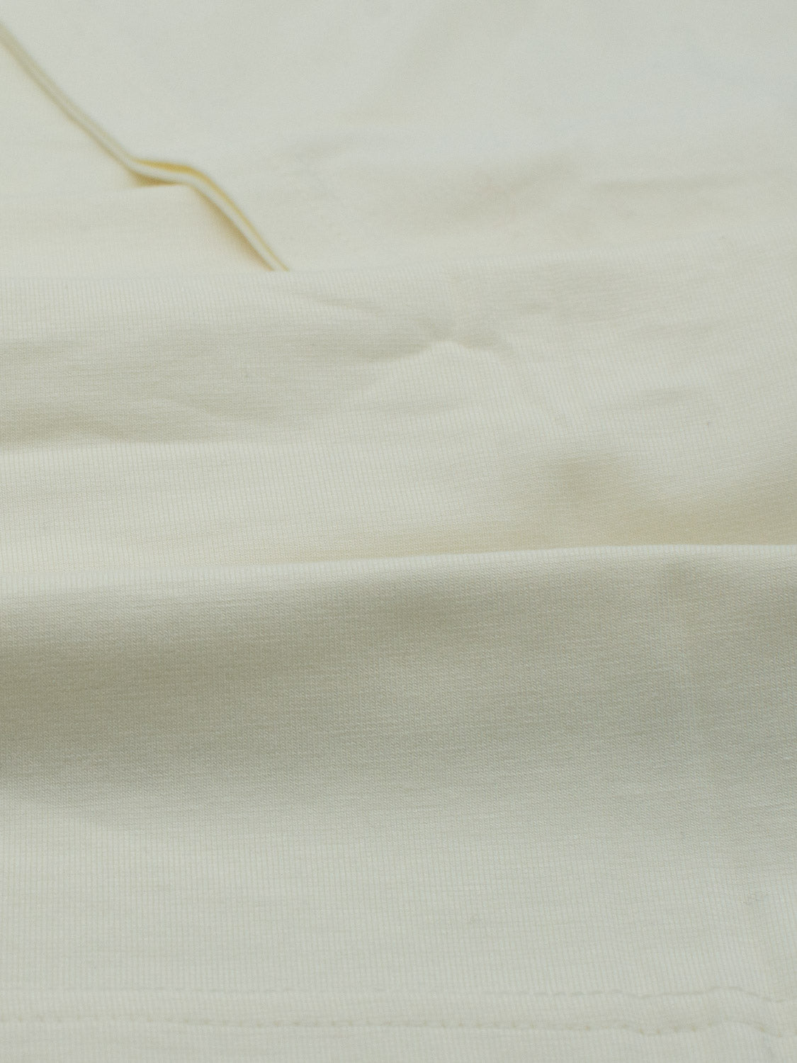 The close-up of off-white, textured fabric with visible seams and subtle wrinkles evokes the feel of ID Menswears Bello Bamboo Blend Rolled Neck Tee, reflecting a soft, natural material symbolic of sustainable clothing.
