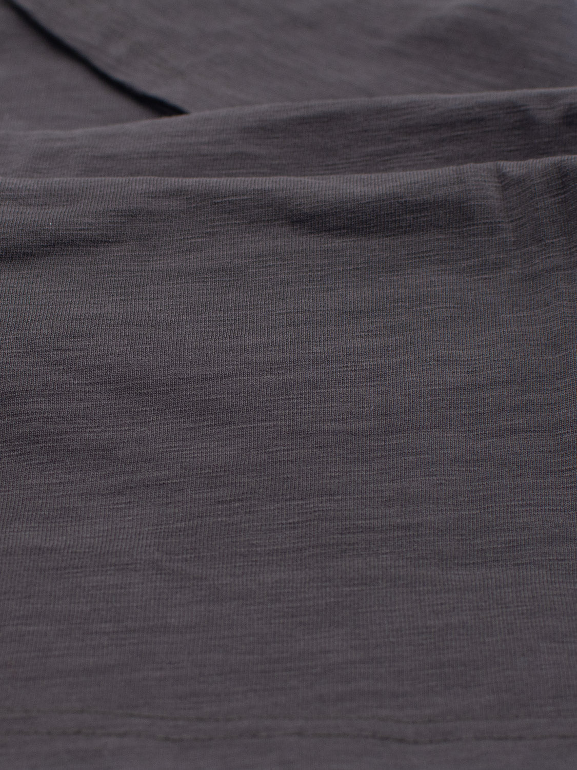 A close-up of the Big Flip Slub Yarn Cotton Tee by ID Menswear reveals folded, dark gray, 100% cotton fabric featuring subtle horizontal lines that give a soft look and slightly crumpled texture.