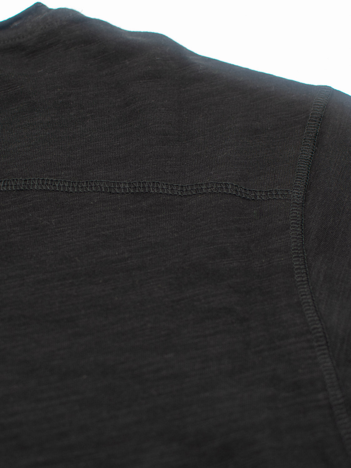 Close-up of a Da Nang Rolled Neck Slub Tee by ID Menswear, highlighting the shoulder and sleeve stitching. The black slub cotton fabric appears soft with a slightly heathered texture, ideal for casual wear.