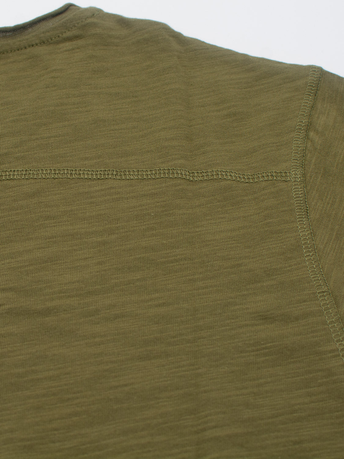 A close-up of the Da Nang Rolled Neck Slub Tee by ID Menswear shows green slub cotton fabric with visible stitching and seam details, highlighting its smooth yet slightly textured appearance, perfect for casual wear.