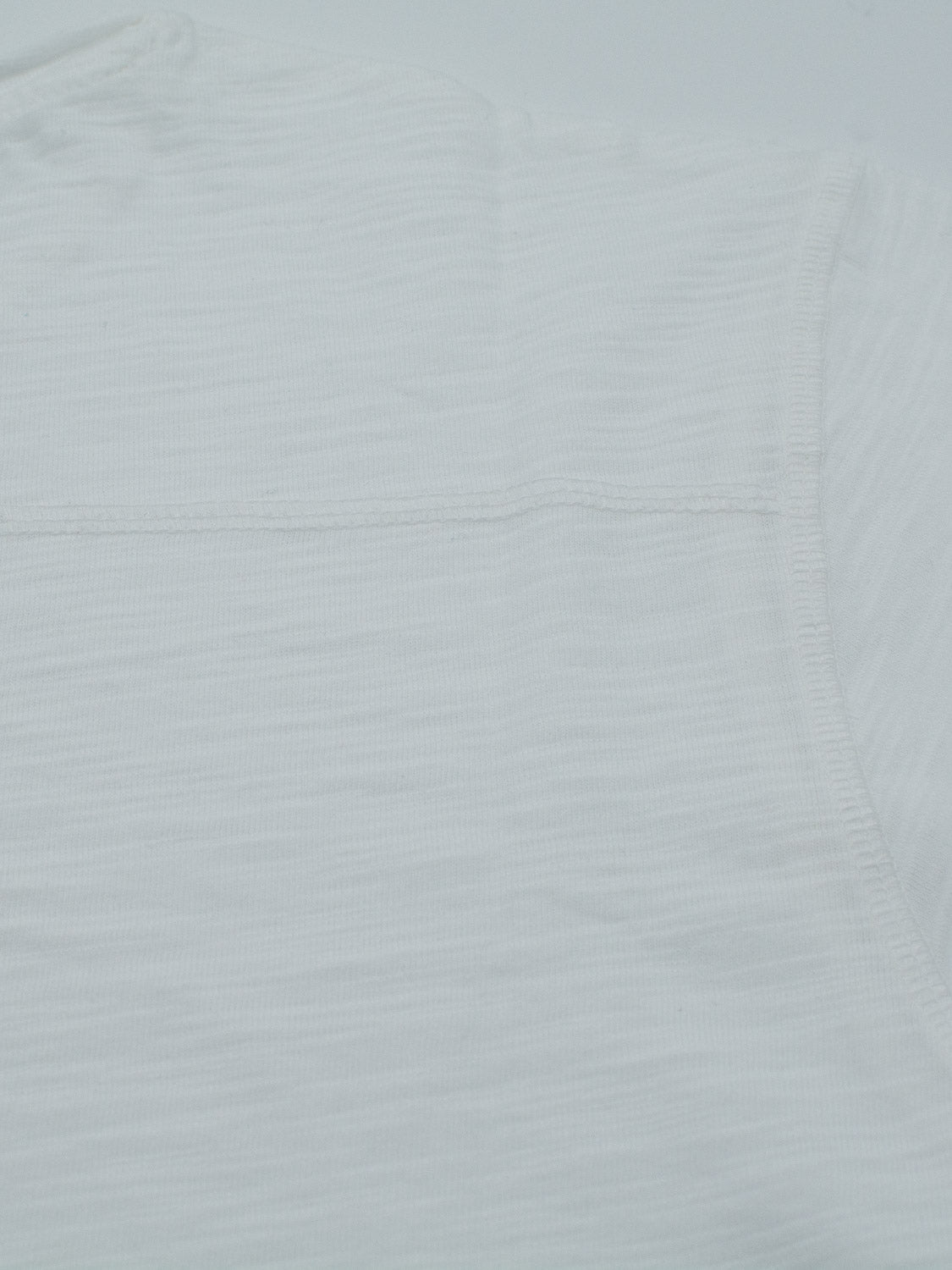 Close-up of the sleeve and shoulder of an ID Menswear Da Nang Rolled Neck Slub Tee, showcasing the slub cotton texture and stitching. The fabric is soft with a slight ribbing, and a horizontal seam is visible.