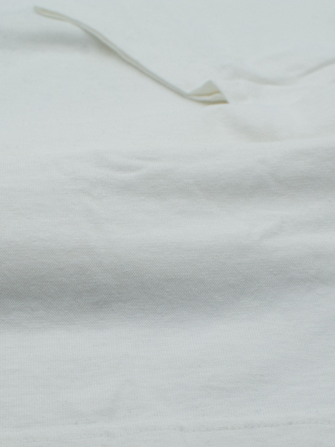 Close-up of ID Menswears Dope Hemp Organic Cotton Tee shows the subtle texture and slight shadowing of the white hemp cotton blend, appearing soft, sustainably crafted, and slightly wrinkled.