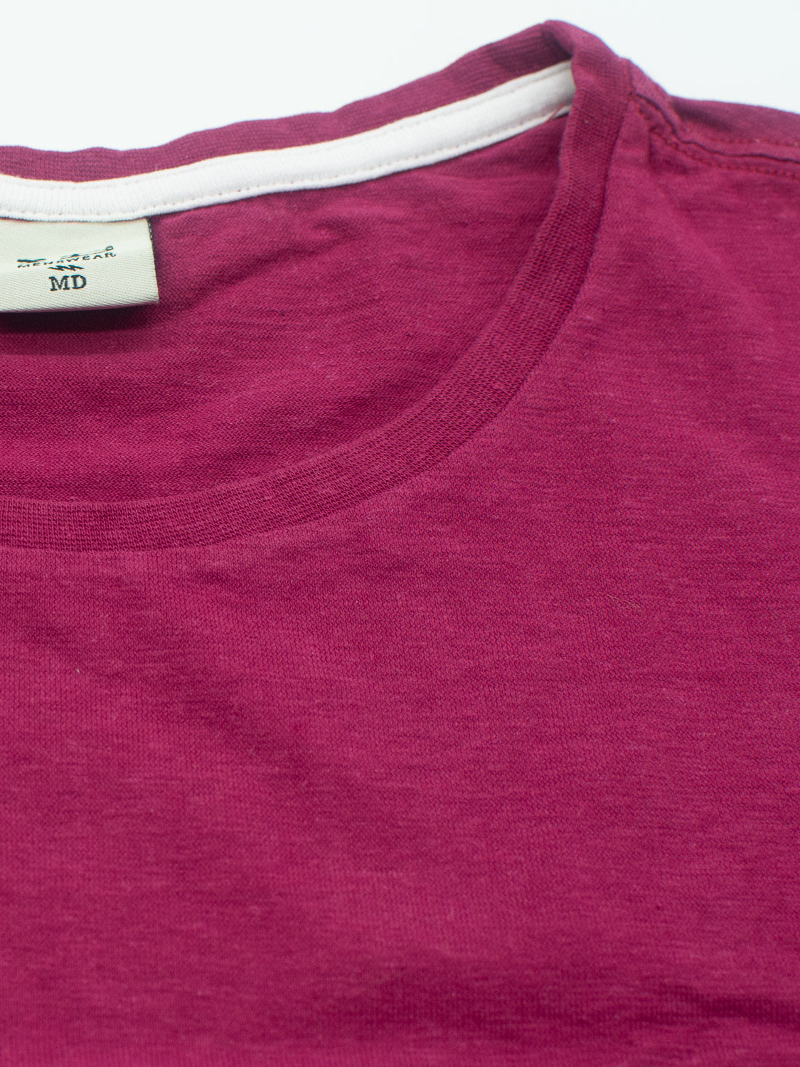 Close-up of a folded Dope Hemp Organic Cotton Tee by ID Menswear, crafted from organic cotton. The maroon fabric is smooth with a visible neckline and an MD tag, placed on a white background.
