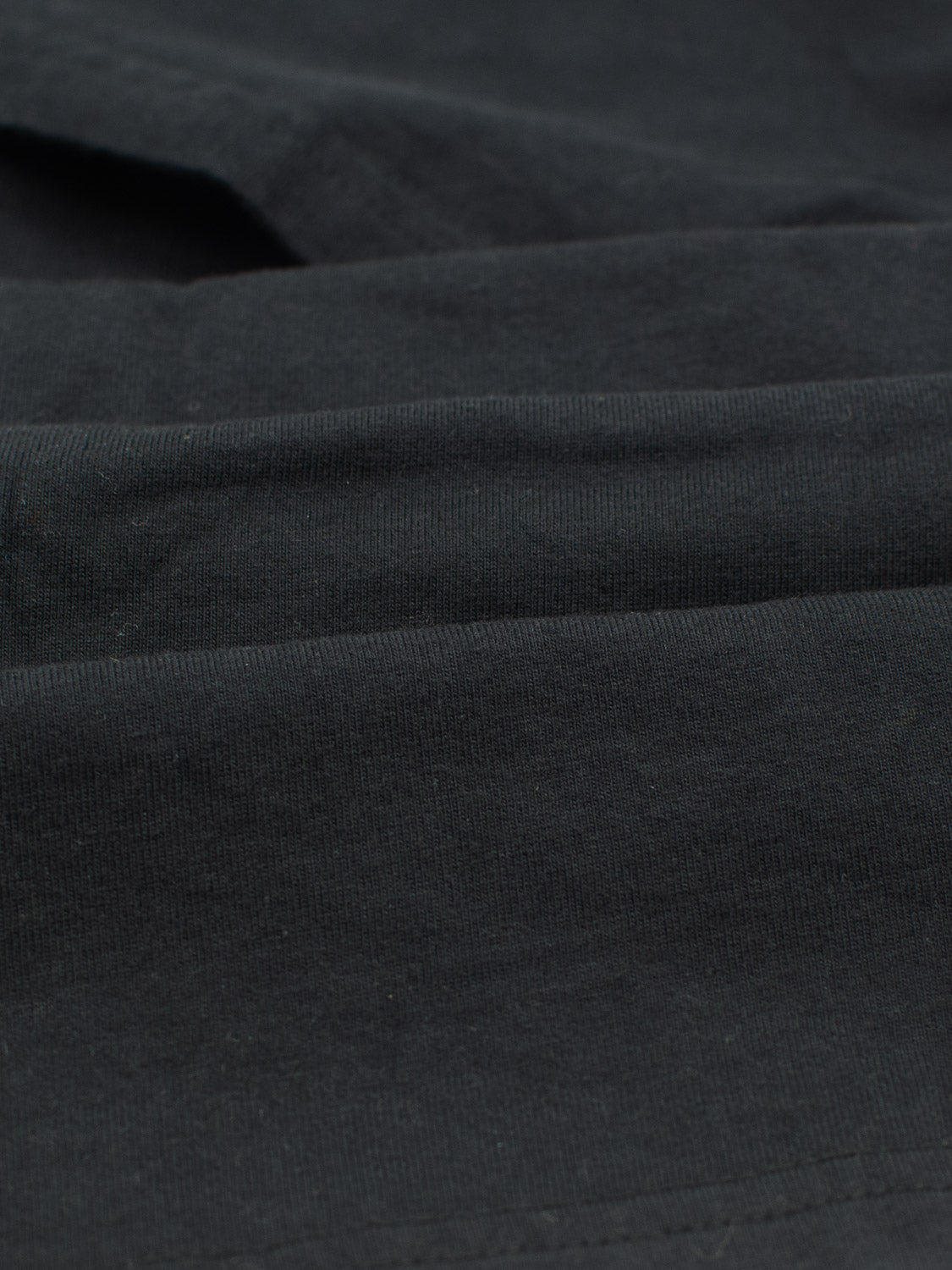A close-up of the Champion Organic Cotton Henley by ID Menswear reveals its textured, soft black cotton jersey fabric. The smooth surface, layered folds, and subtle shadows and highlights showcase its depth.