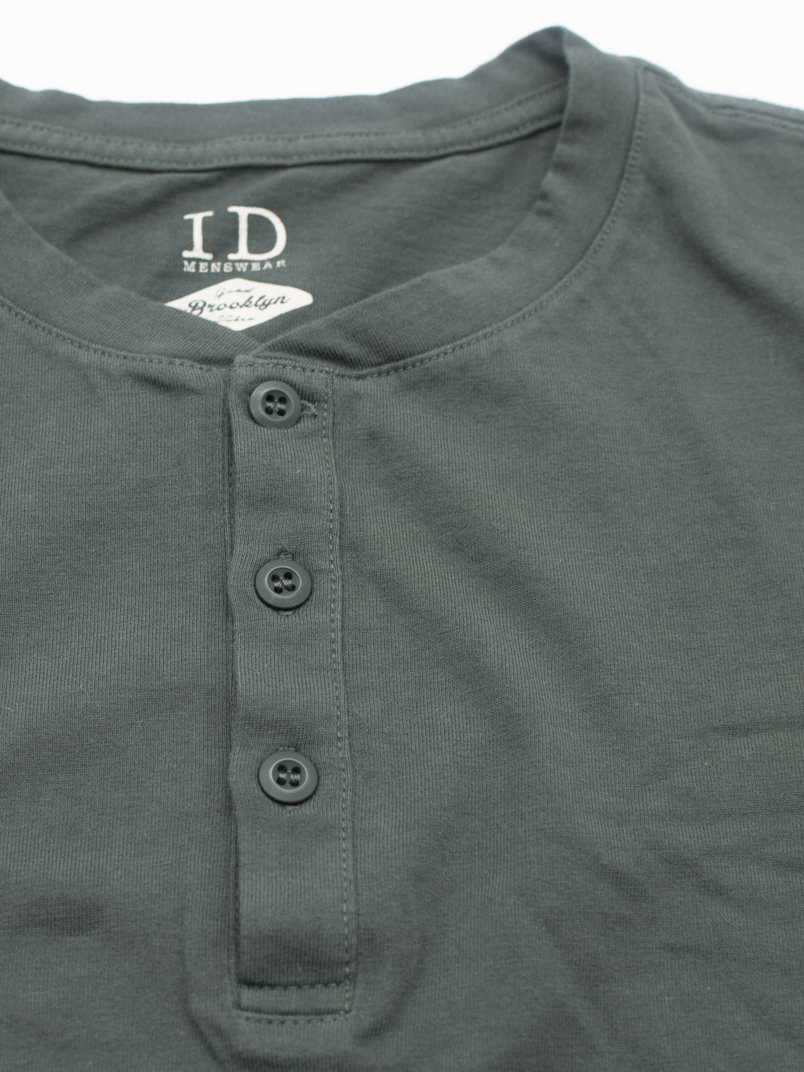 A dark green henley shirt, the Champion Organic Cotton Henley by ID Menswear, is laid flat. Crafted from organic cotton jersey, it features a three-button placket and a round neckline, embodying a classic silhouette.