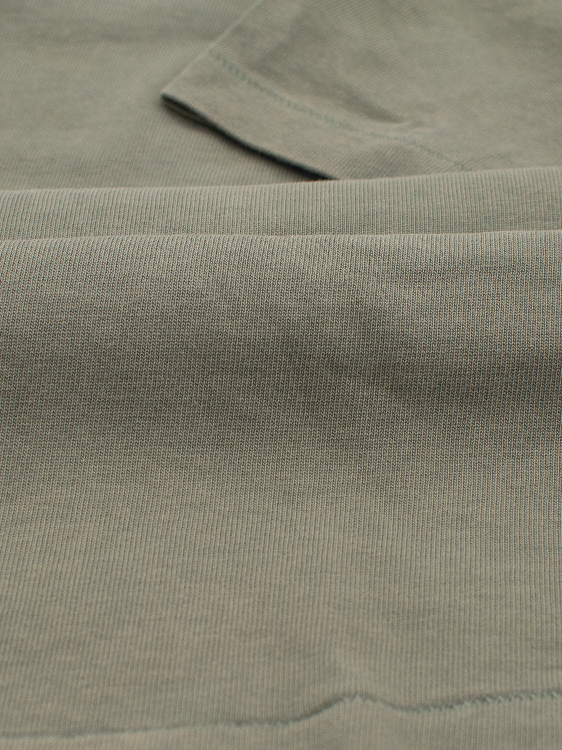 Close-up of the Freeman Organic Vintage Wash Tee by ID Menswear, showcasing its textured green fabric with visible ridges evoking a vintage worn look, and the folded fabric highlights its texture and color variations.