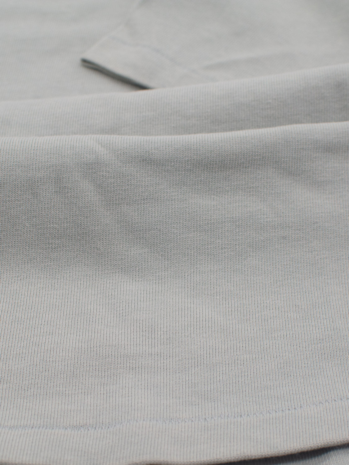 Close-up of the soft, light blue Freeman Organic Vintage Wash Tee by ID Menswear, featuring a subtle ribbed texture and a vintage worn look. The folds highlight its smooth, fine weave.