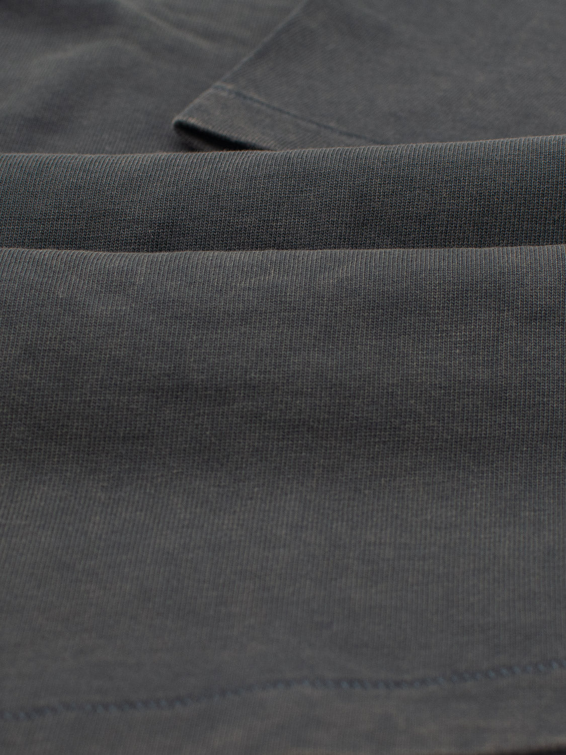 Close-up of Freeman Organic Vintage Wash Tee by ID Menswear, featuring dark gray fabric with visible seams and a soft, slightly ribbed texture that offers a vintage worn look and timeless character.