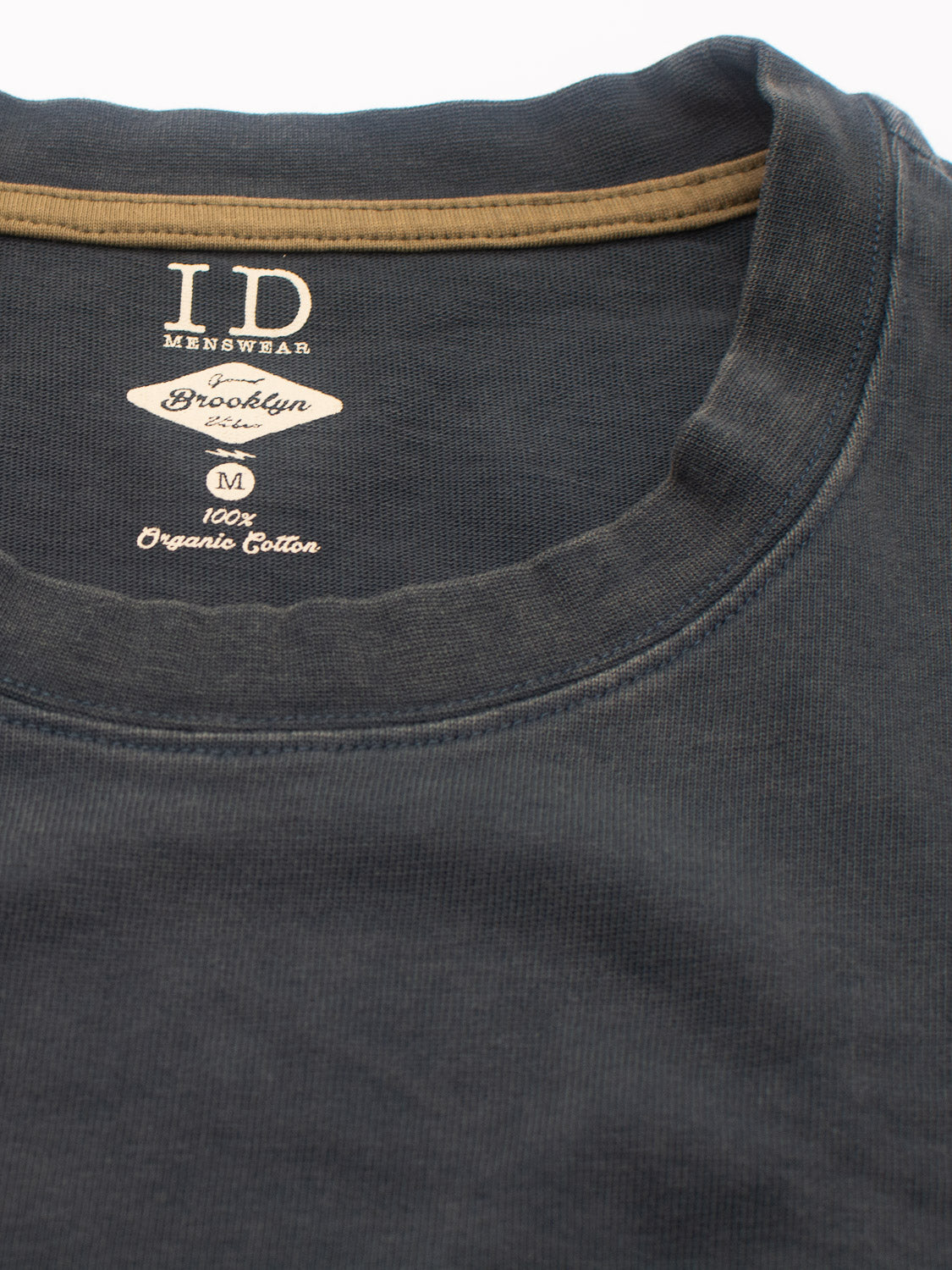 Close-up of the Freeman Organic Vintage Wash Tee in dark gray with a contrasting brown collar, showcasing its vintage worn look. Inside label reads ID Menswear and Brooklyn. Made from 100% organic cotton, it embodies sustainable style with timeless appeal.