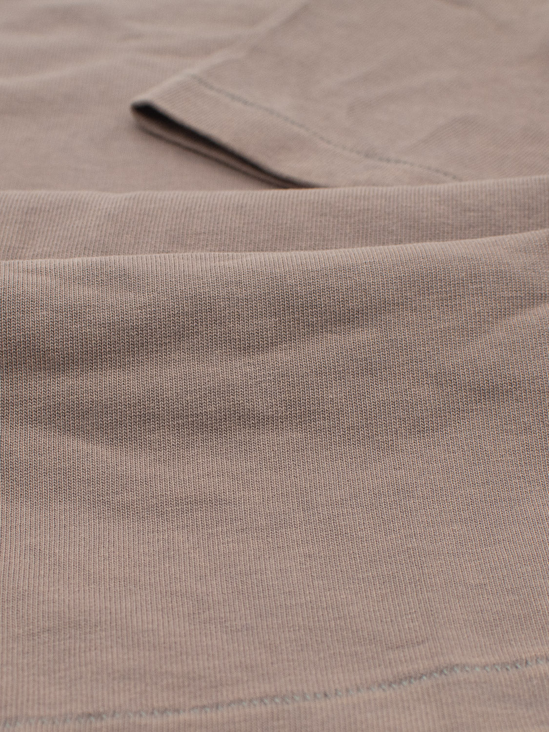 Close-up of the Freeman Organic Vintage Wash Tee by ID Menswear, made from beige ribbed organic cotton. The fabric appears smooth and soft, with subtle lighting highlighting its natural folds and details.