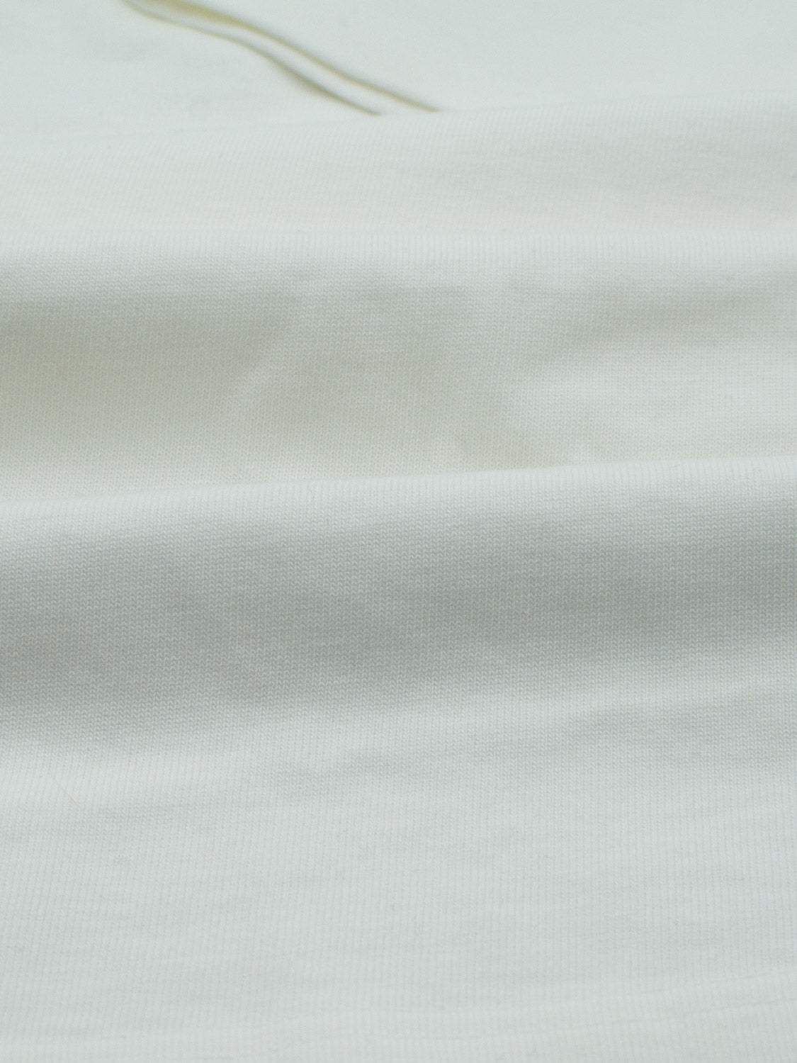 Close-up of the light beige fabric of the ID Menswears City Organic Cotton Tee, featuring a ribbed texture and gentle folds. Its soft and smooth appearance highlights its eco-friendly, slim-fit design made from organic cotton.