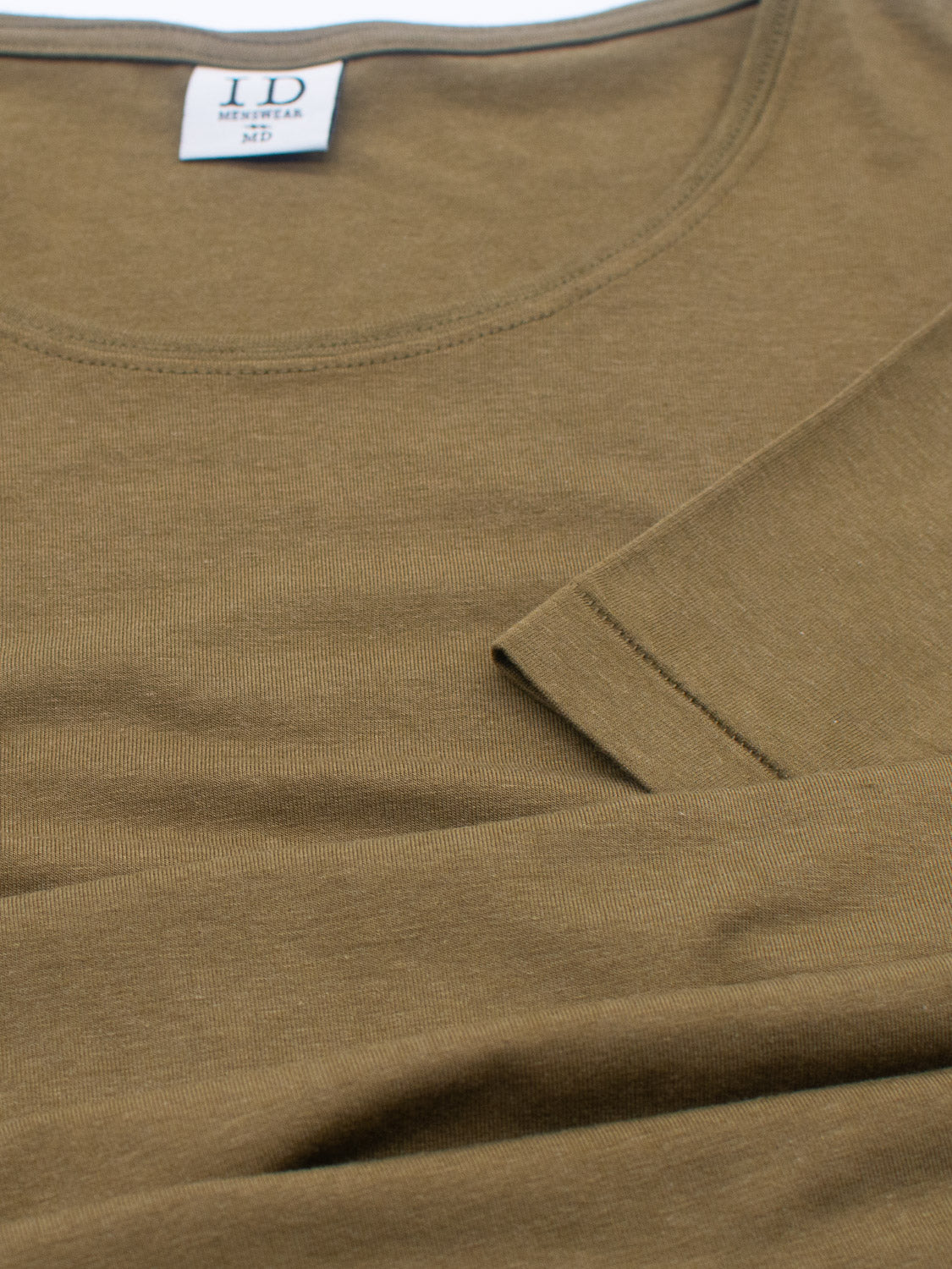 Close-up of a folded brown ID Menswear Slay Wide Neck Bamboo Blend Tee with a round neckline, featuring a white label inside the collar with LD and Medium printed on it. Crafted from organic cotton, the fabric appears smooth and neatly arranged.
