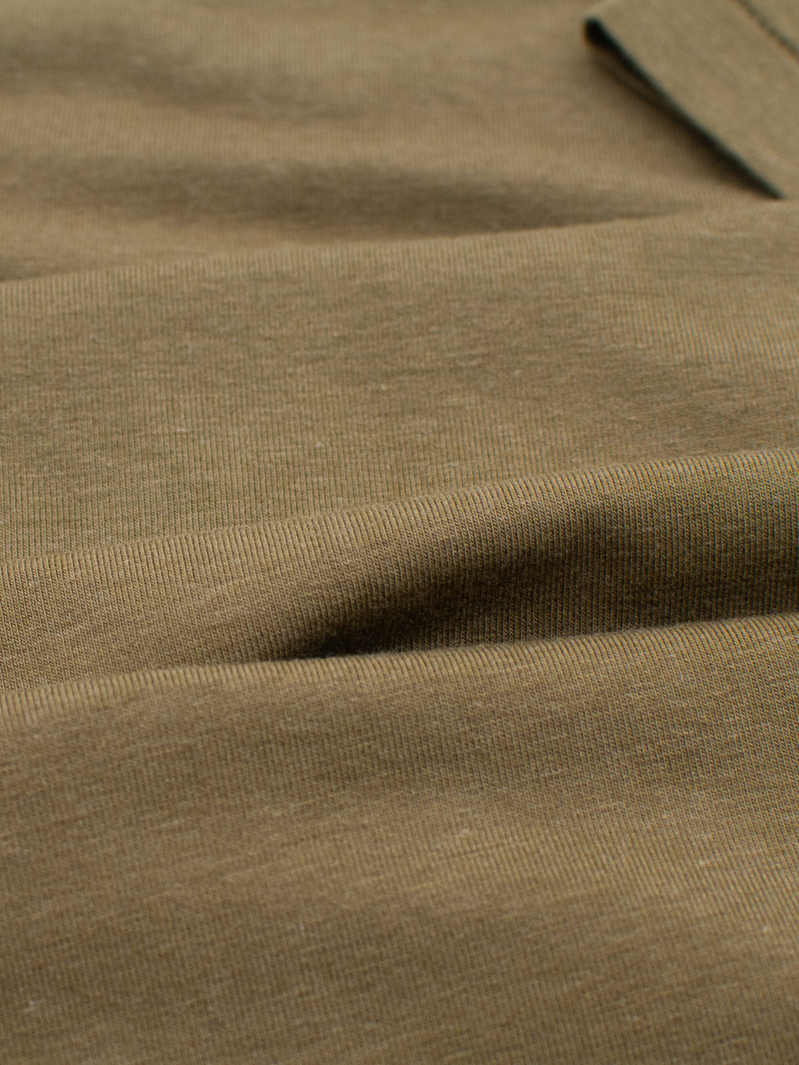 A close-up of the Slay Wide Neck Bamboo Blend Tee by ID Menswear reveals its textured, olive-colored fabric with subtle horizontal ridges. Made from organic materials, it appears soft and smooth, highlighting its weave and quality in natural light.